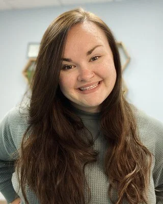 Erin wearing a gray top, indoors with a blurred background.