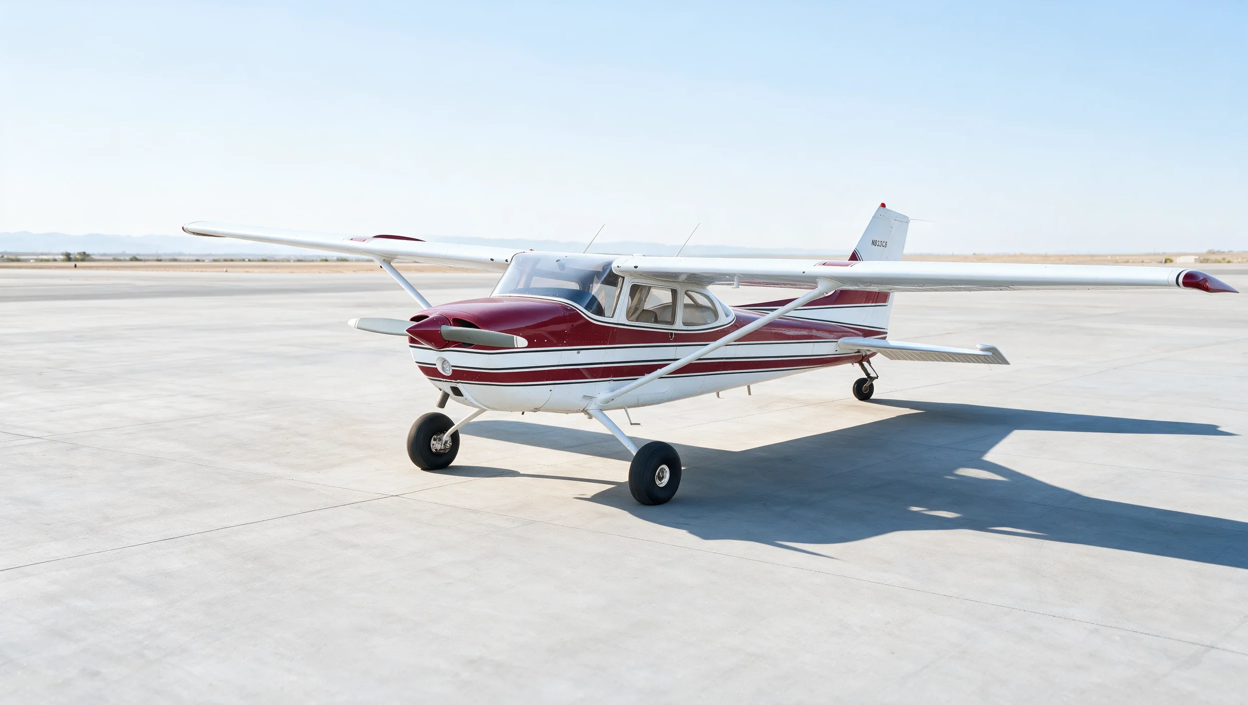 A small white and red propeller airplane parked on a concrete tarmac under a clear blue sky.