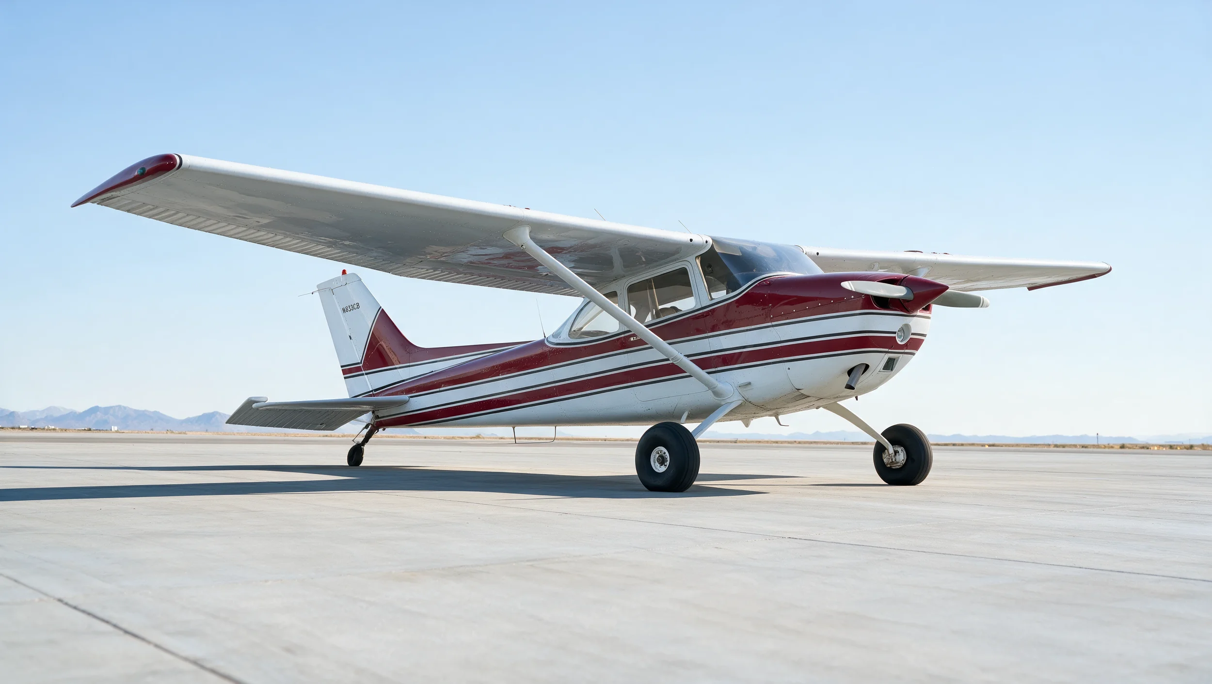 Small private airplane with white and red design parked on an empty runway.