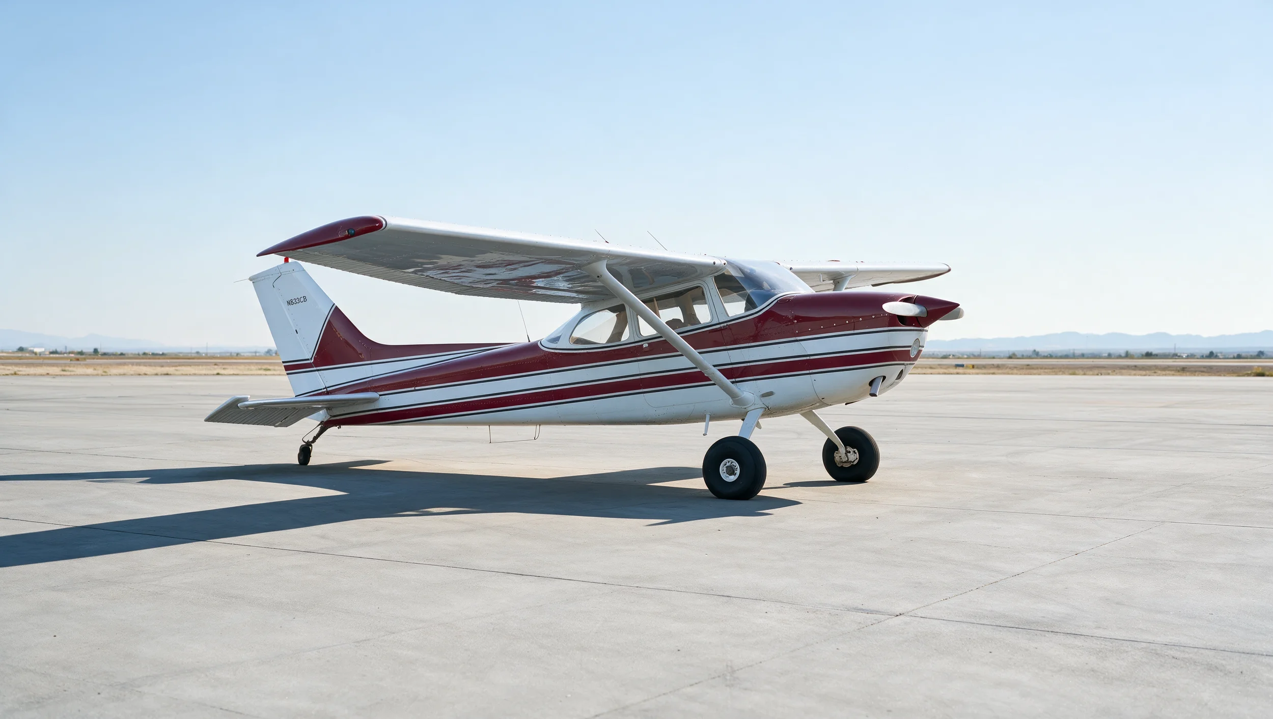 Small propeller airplane with red and white stripes parked on a concrete runway.