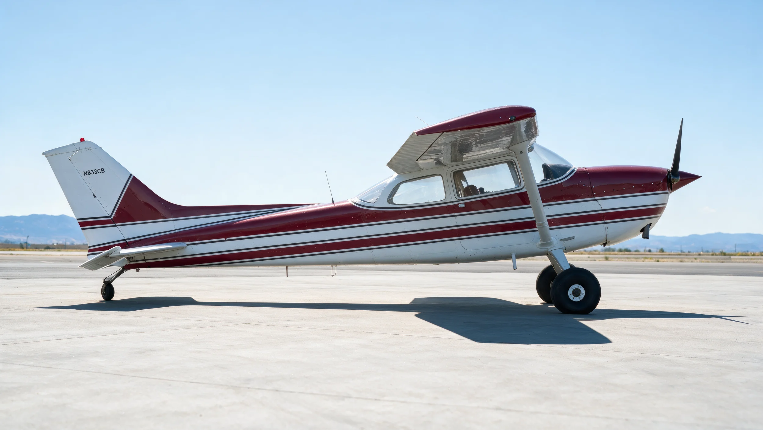 Small red and white single-engine propeller airplane on an airport tarmac.