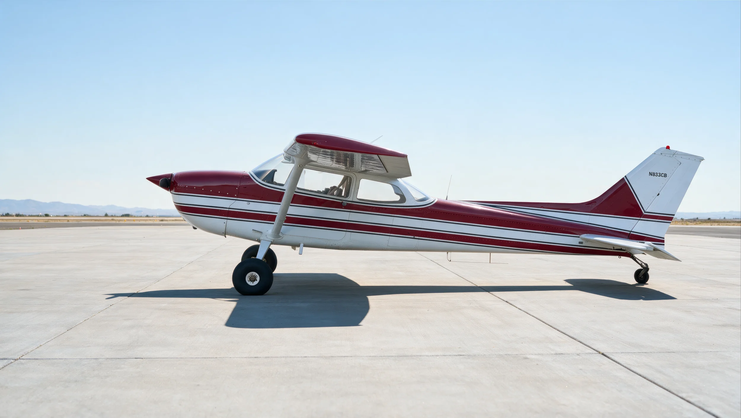 Small red and white single-engine airplane parked on a concrete tarmac with a clear blue sky in the background.