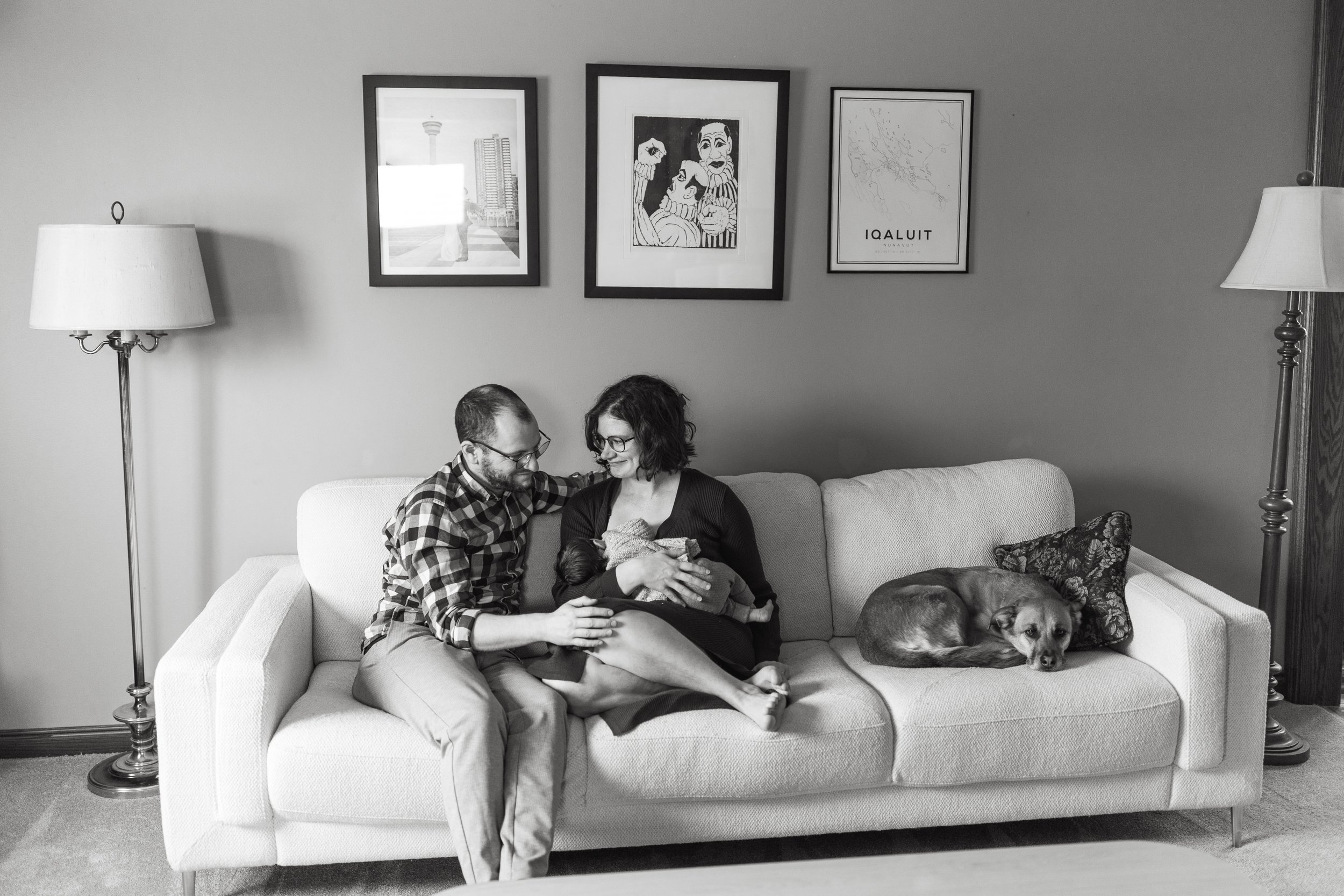 Candid black and white photo of couple at home on the couch with their newborn baby and dog