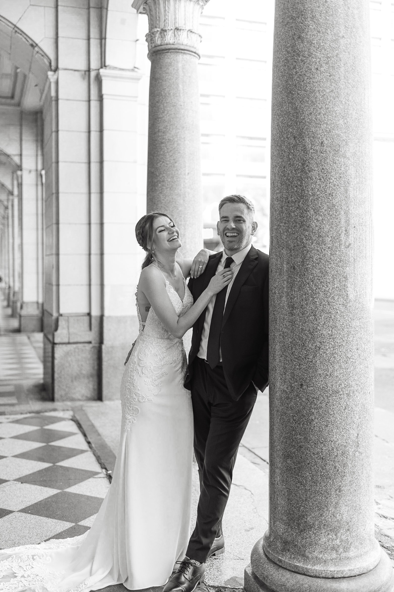 Bride and groom laughing near stone columns in black and white photo in Downtown Calgary