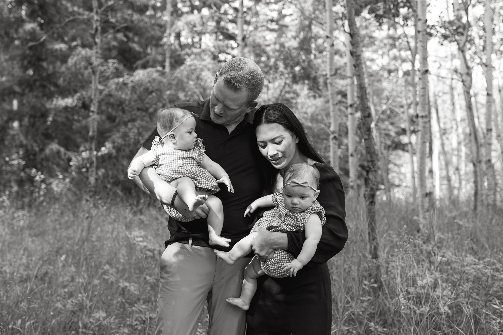 Candid black and white photo of mother and father holding their twin daughters during lifestyle family session in Calgary