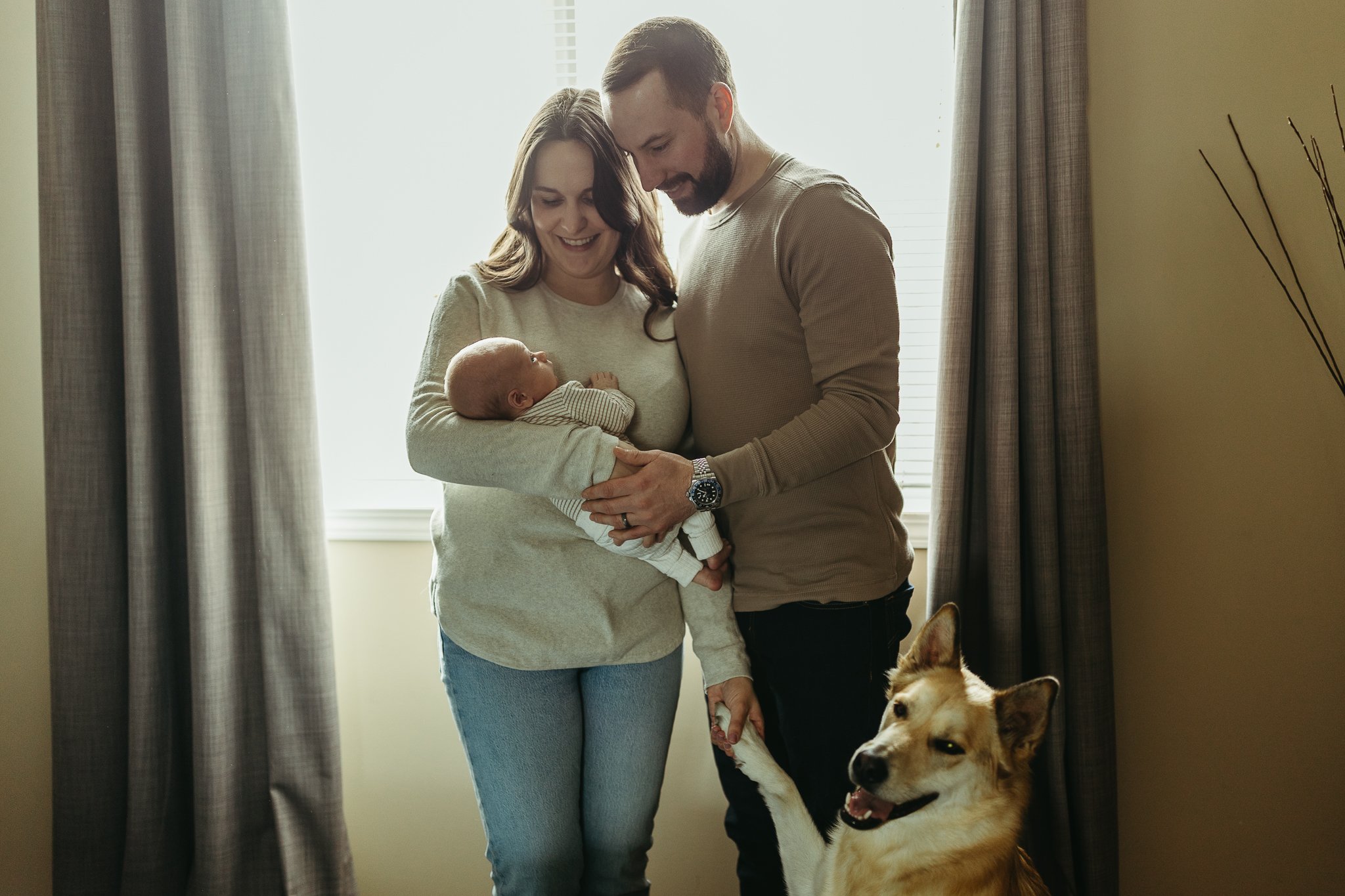 New mom and dad hold their newborn baby at home in Calgary with their shepherd dog