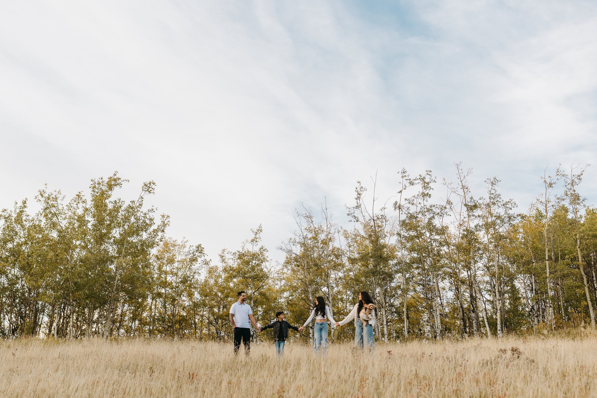 Family stands in the dry grass during candid fall family photo shoot in Calgary