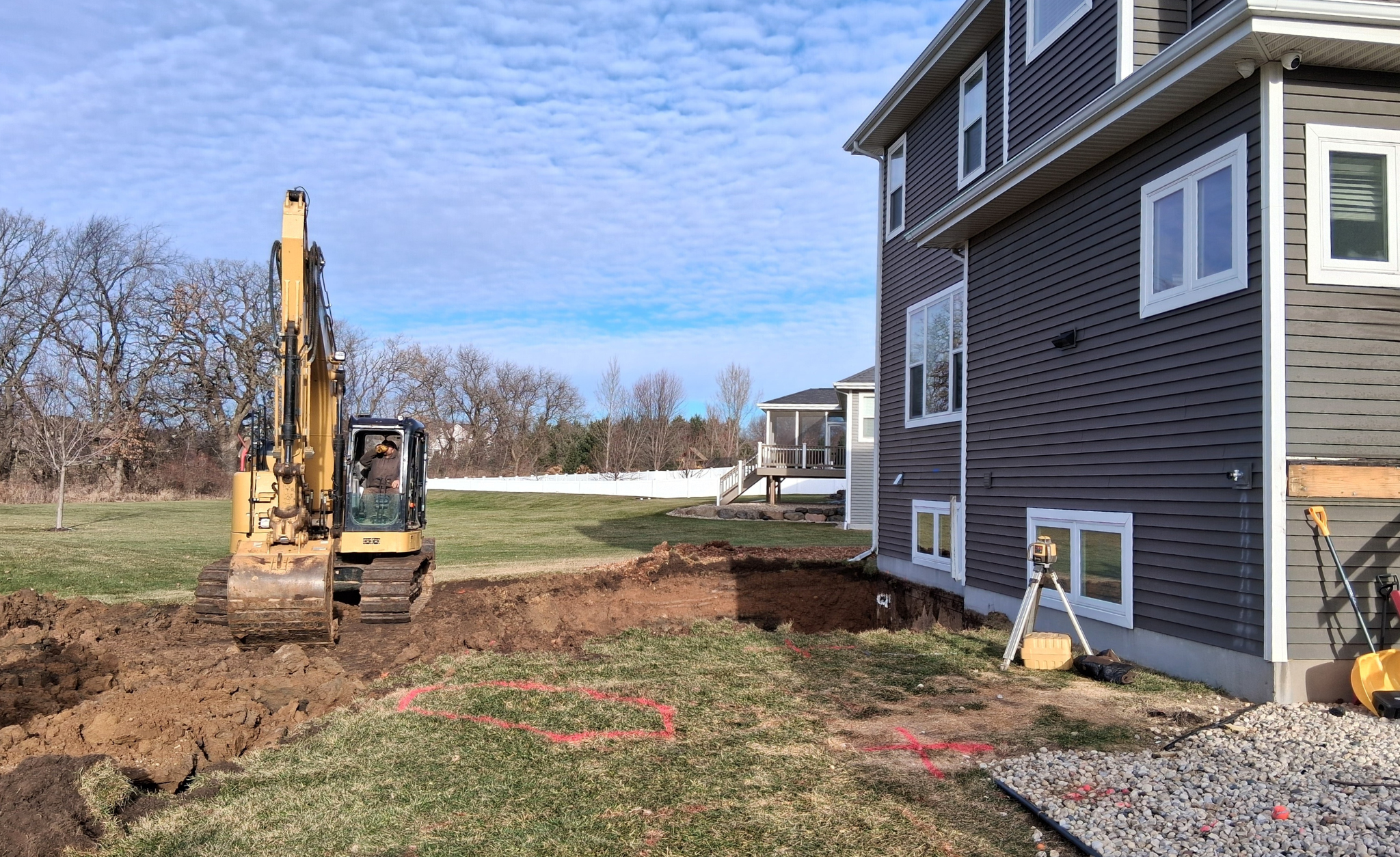 Home addition under construction with excavation beside an existing house, showing the early stages of a major home renovation.