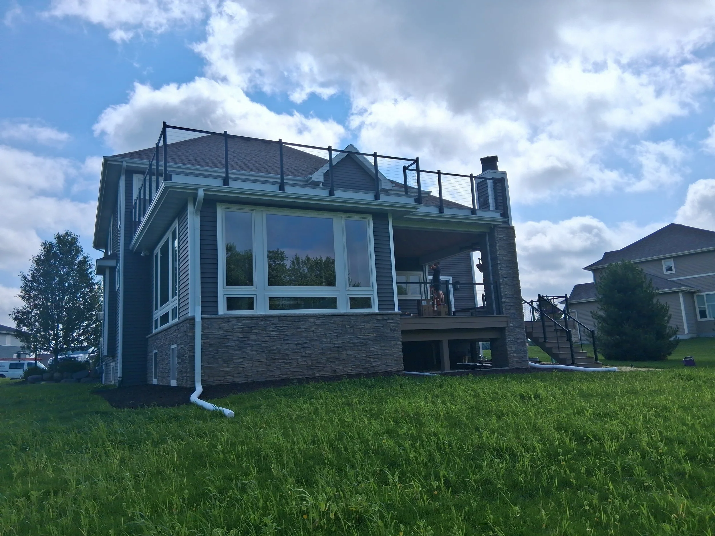 Modern two-story custom home with gray siding, stone facade, large windows, and rooftop deck in Madison, WI.