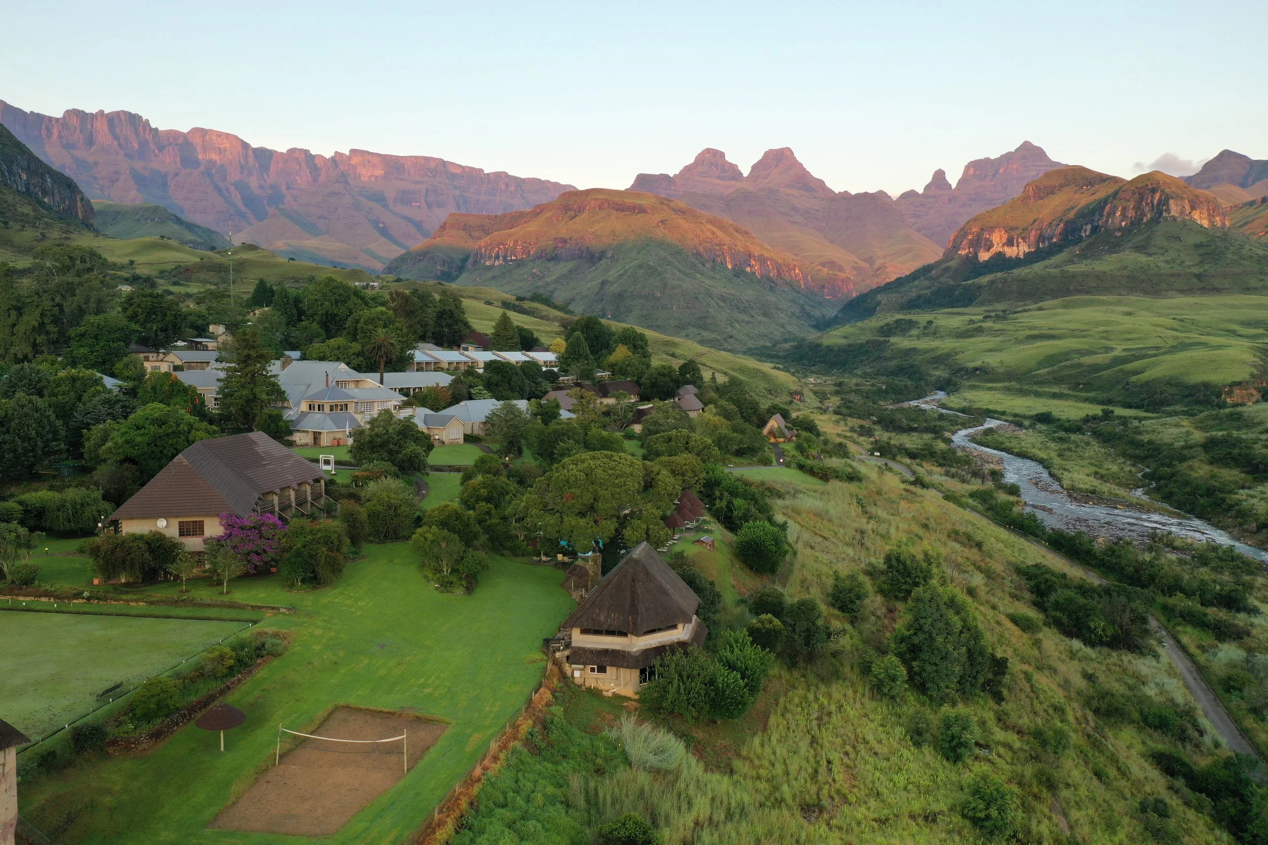A scenic view of a lush green valley with residential buildings, surrounded by mountains and a river flowing through the landscape.