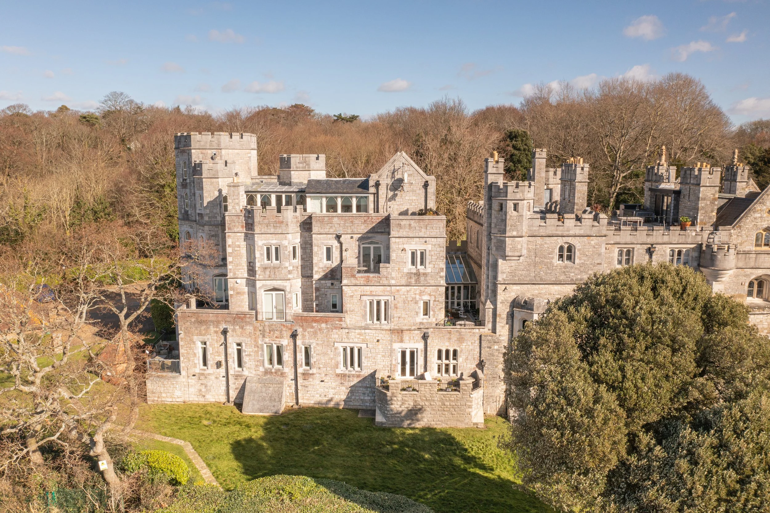 An aerial view of the Netley castle with multiple towers, surrounded by trees and greenery under a partly cloudy sky.