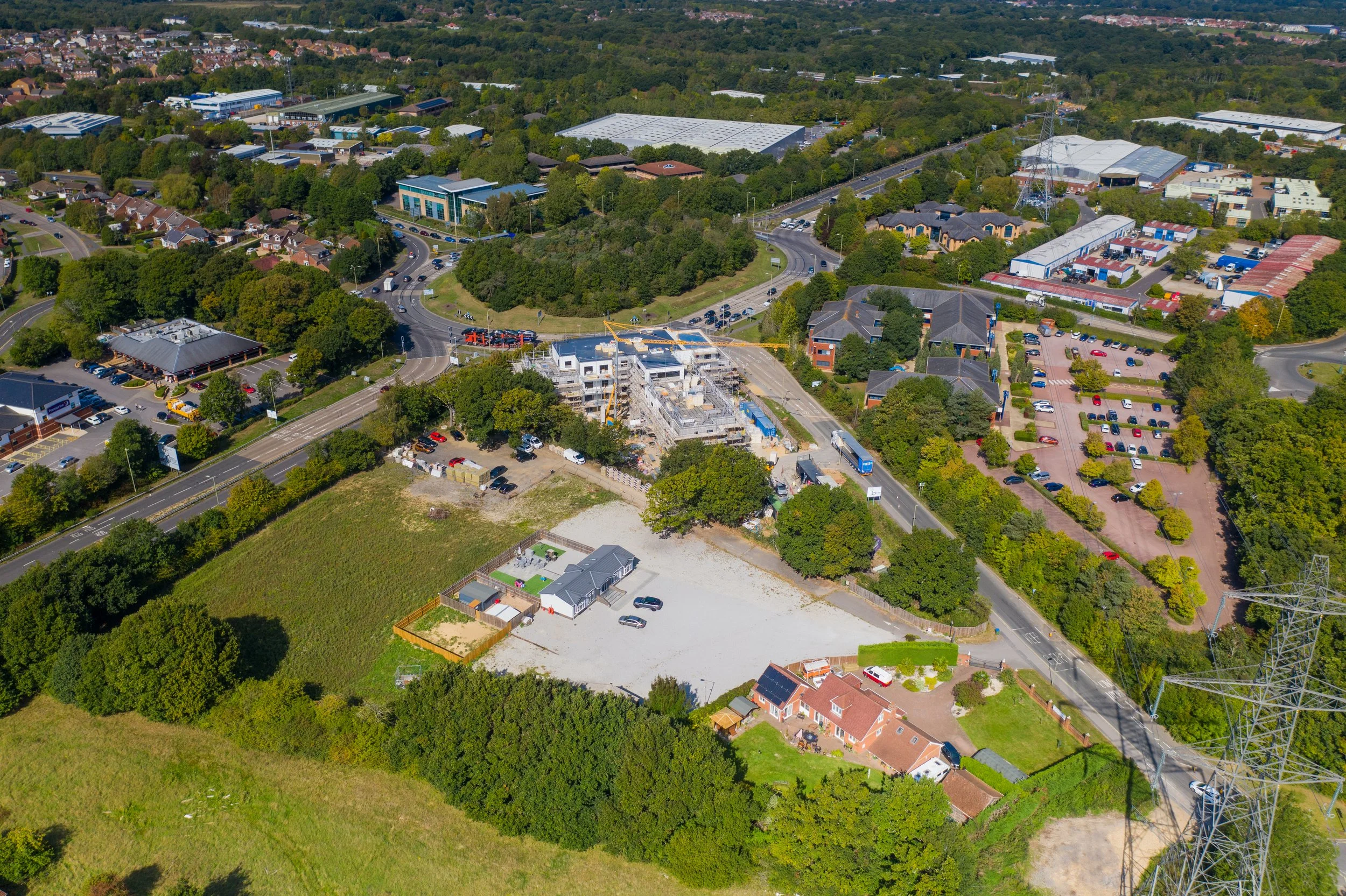 Aerial view of a suburban area with a mix of commercial buildings, residential houses, parking lots, and construction site with cranes.