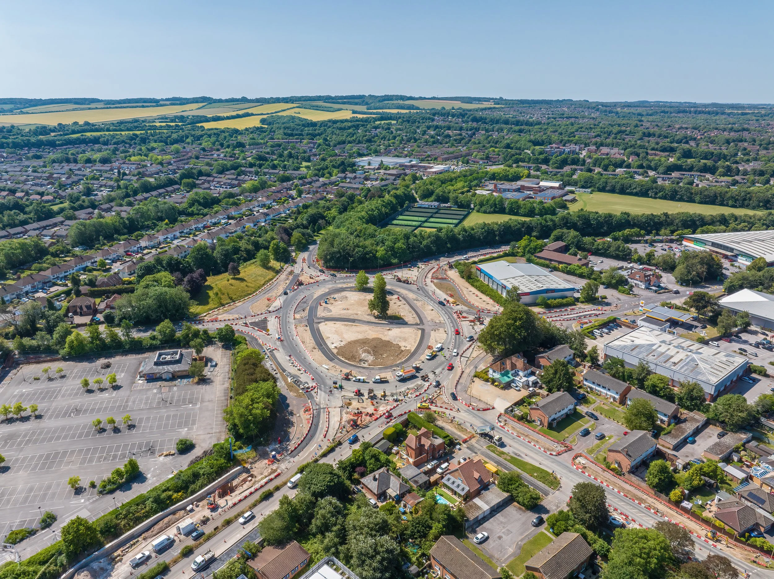 Aerial view of a circular road construction site with surrounding residential and commercial buildings, parking lots, and green spaces.