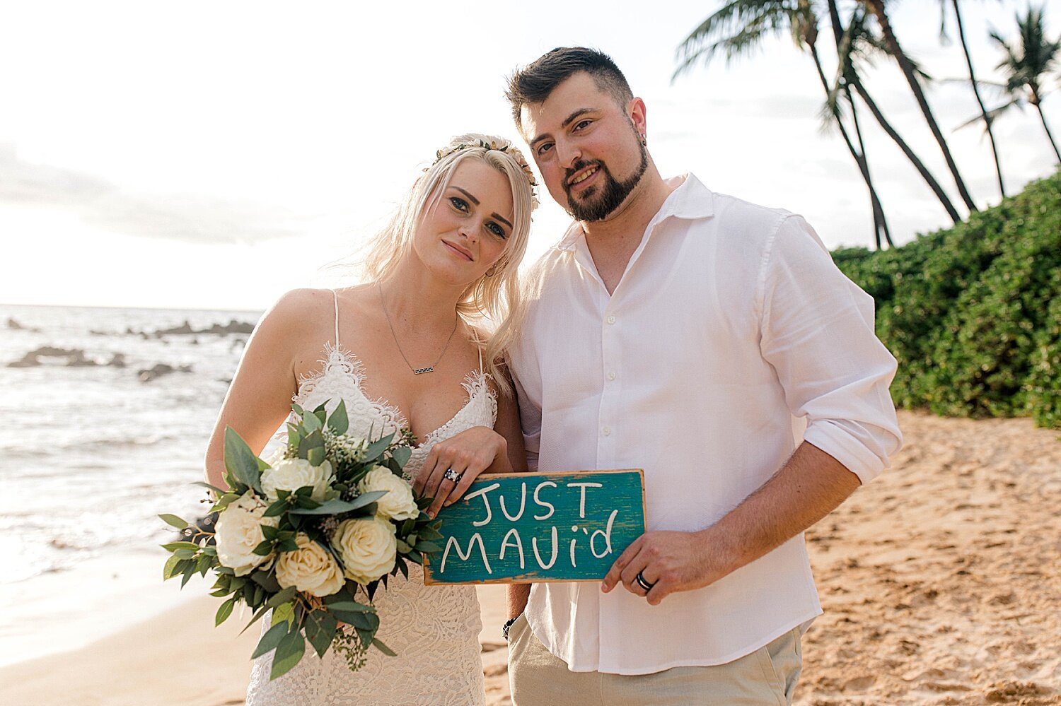 Bride and groom posing with "Just Mauid" sign following Maui beach elopement ceremony