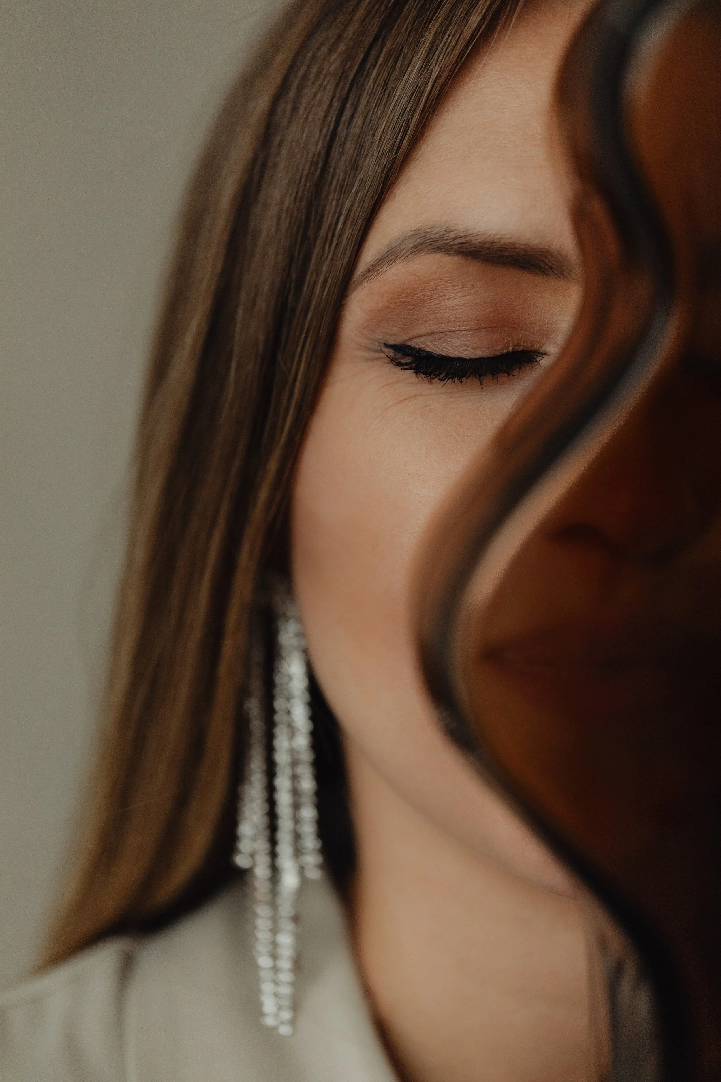 Woman with eyes closed beside a violin, wearing long dangling earrings.