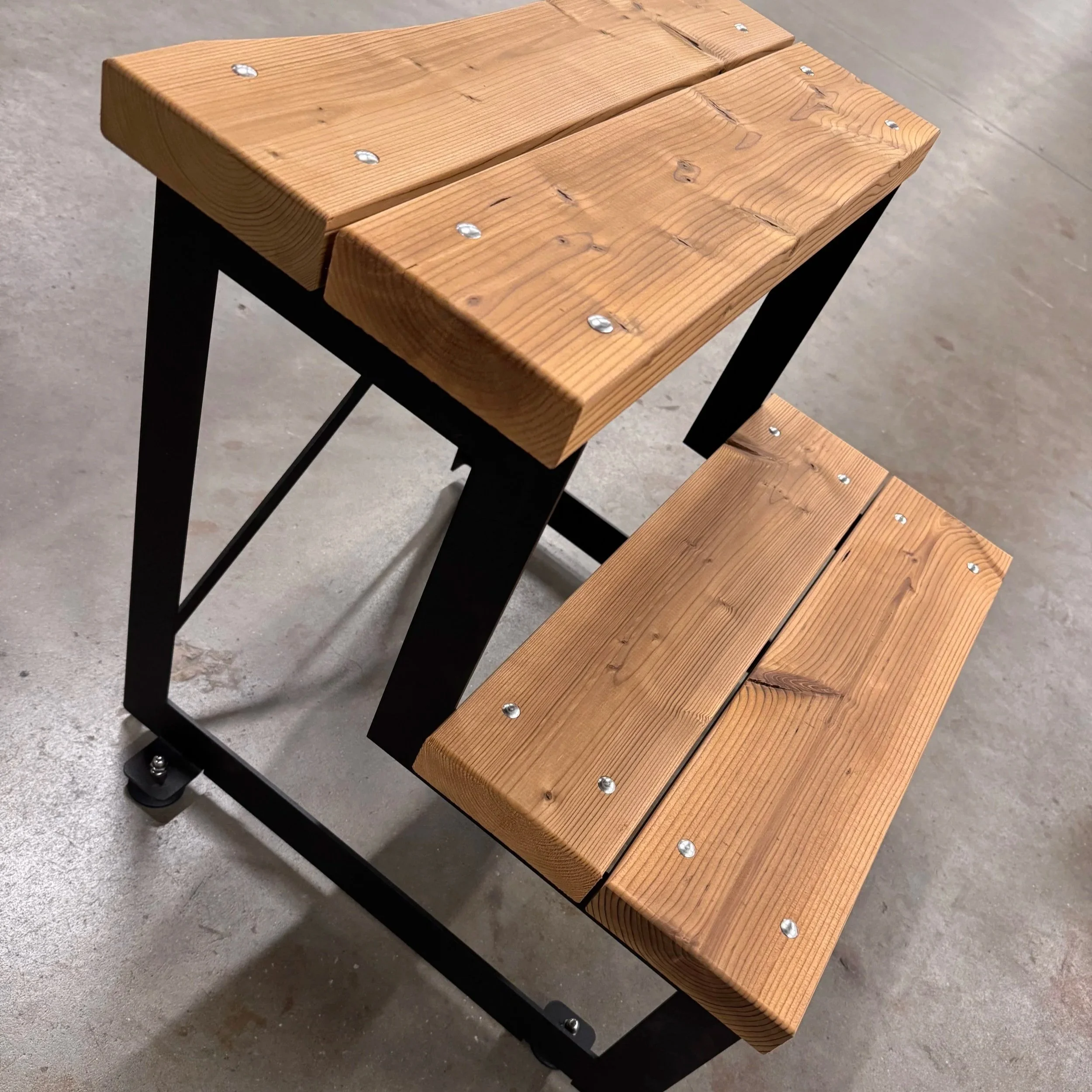 Een houten bank met een zwart metalen frame, geplaatst op een betonnen vloer.