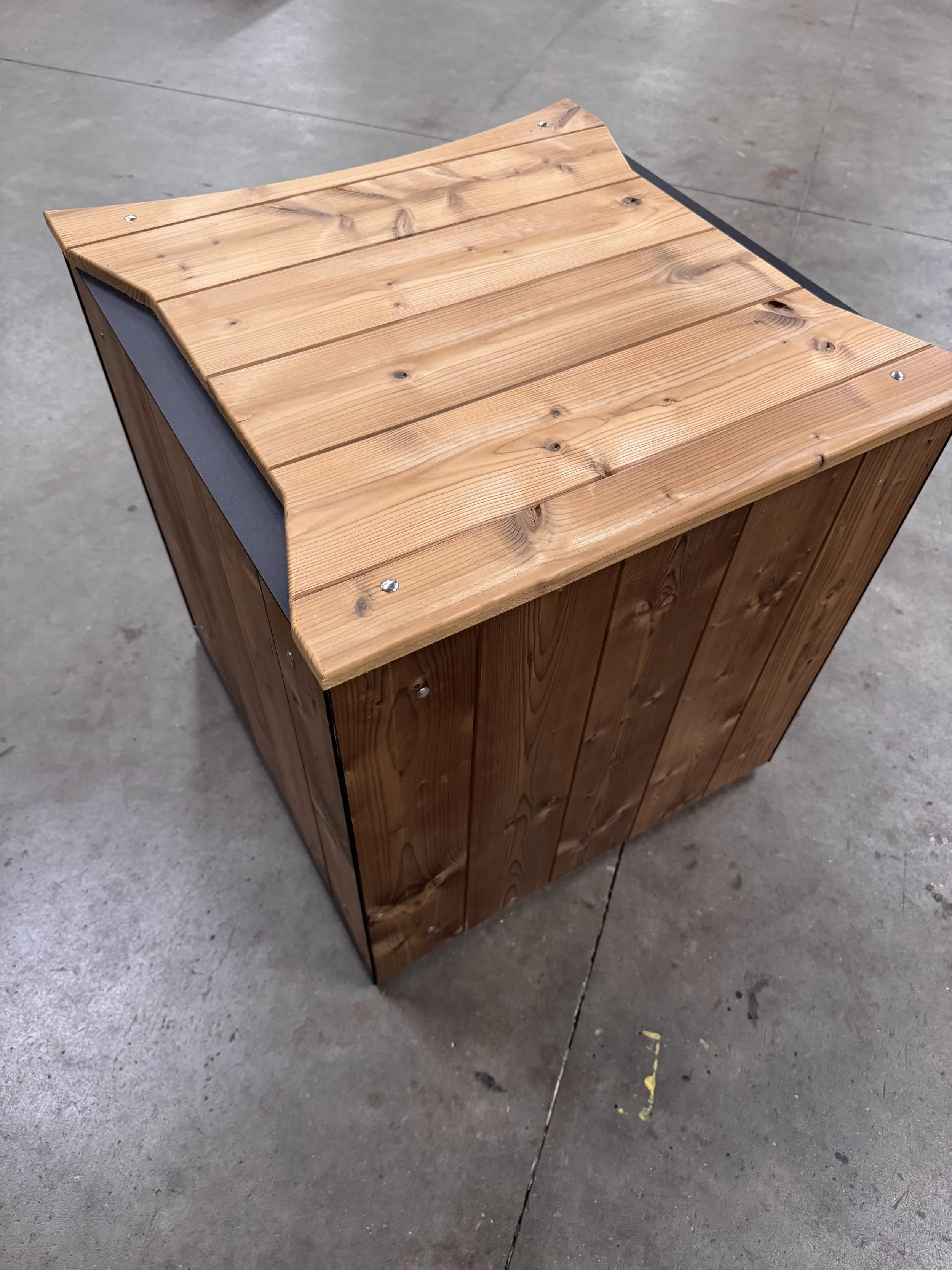 Een houten bank met een afgeronde zijkant staat op een betonnen vloer.