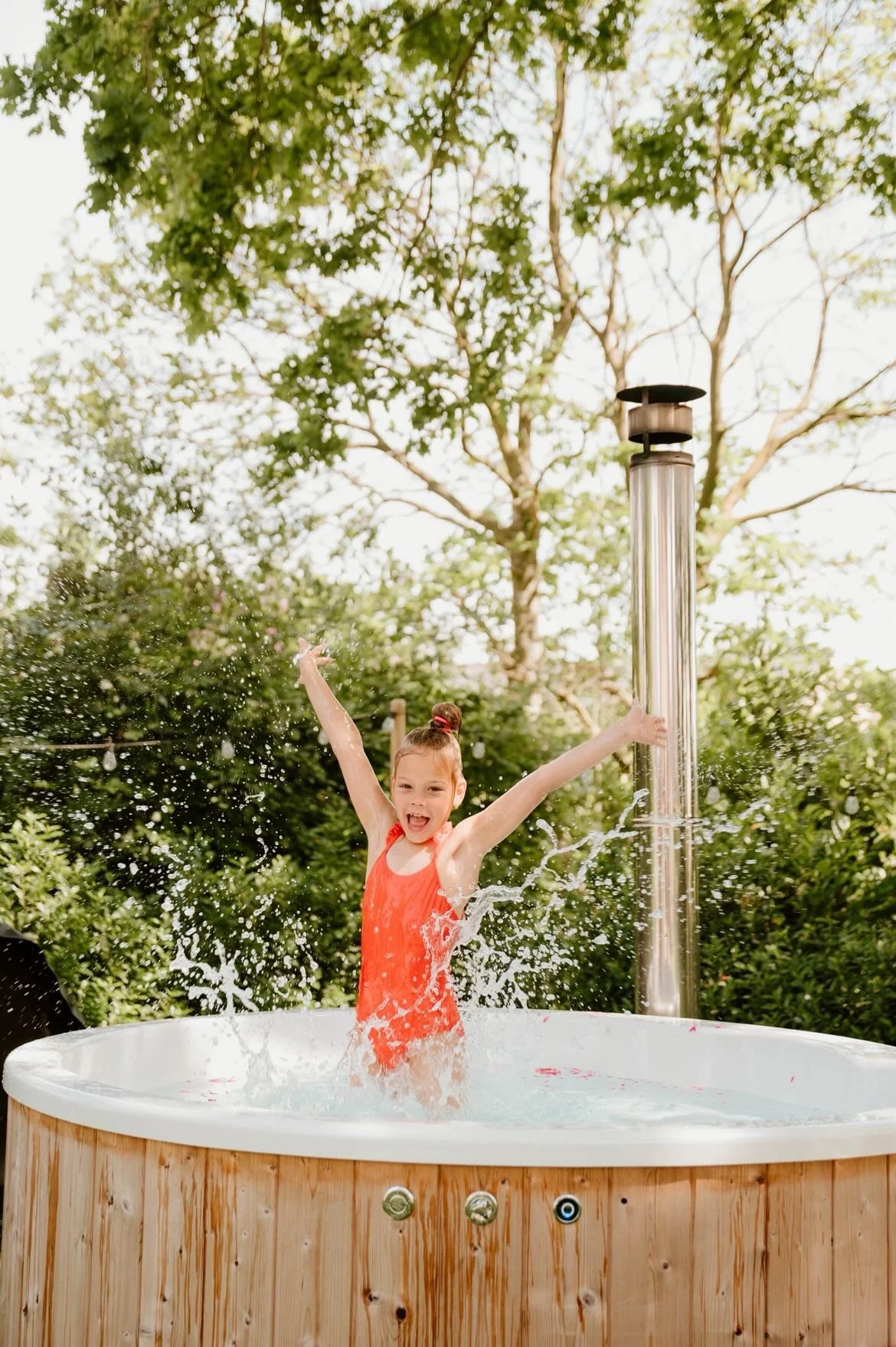 Meisje speelt in een hottub gebowud door Wellnez Atelier onder een waterval in een groene tuin