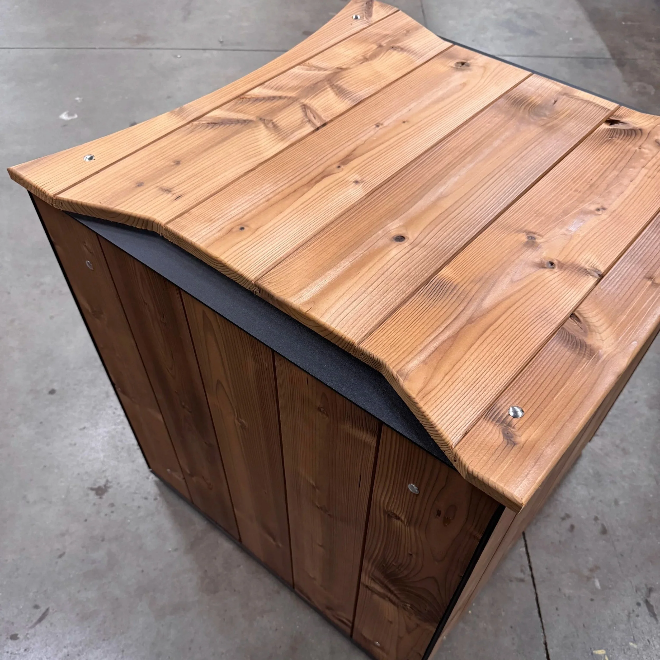Een houten meubelstuk met een houten blad en metalen poten, geplaatst op een betonnen vloer.