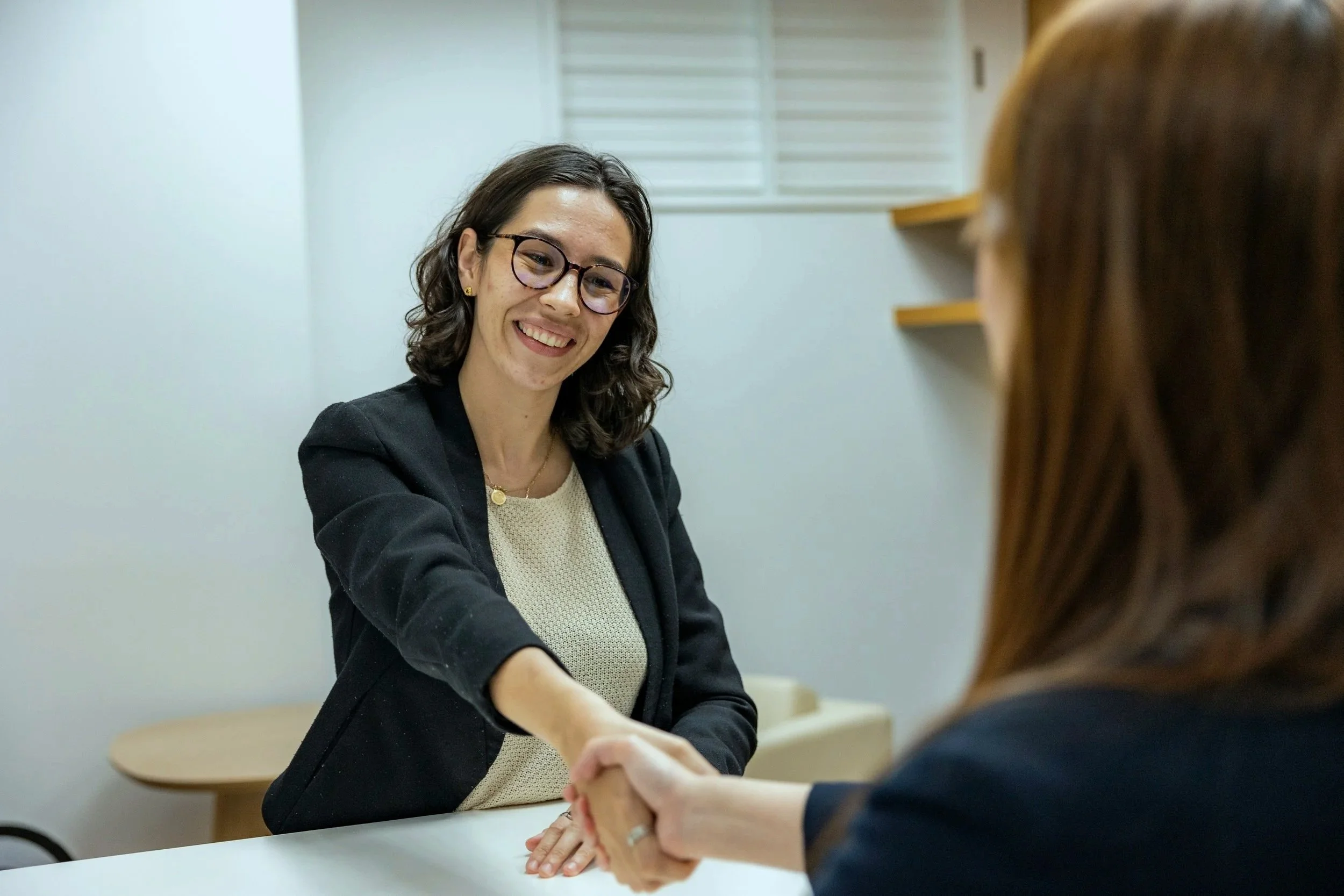 A female candidate shakes hands with her interviewer after receiving news that she got hired for the open position she applied to.