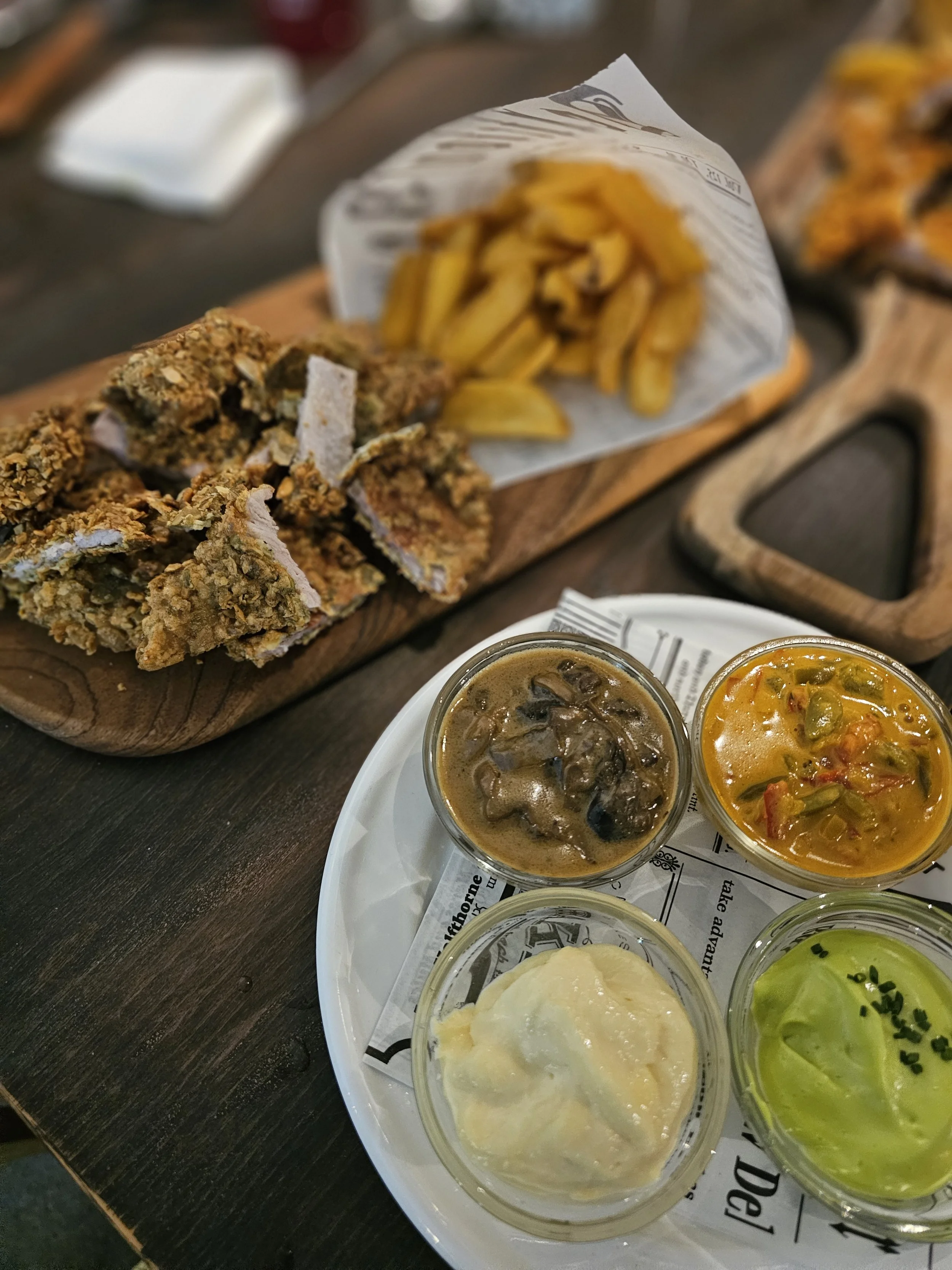 Fried chicken strips with French fries, assorted dipping sauces in small bowls, on a wooden table.