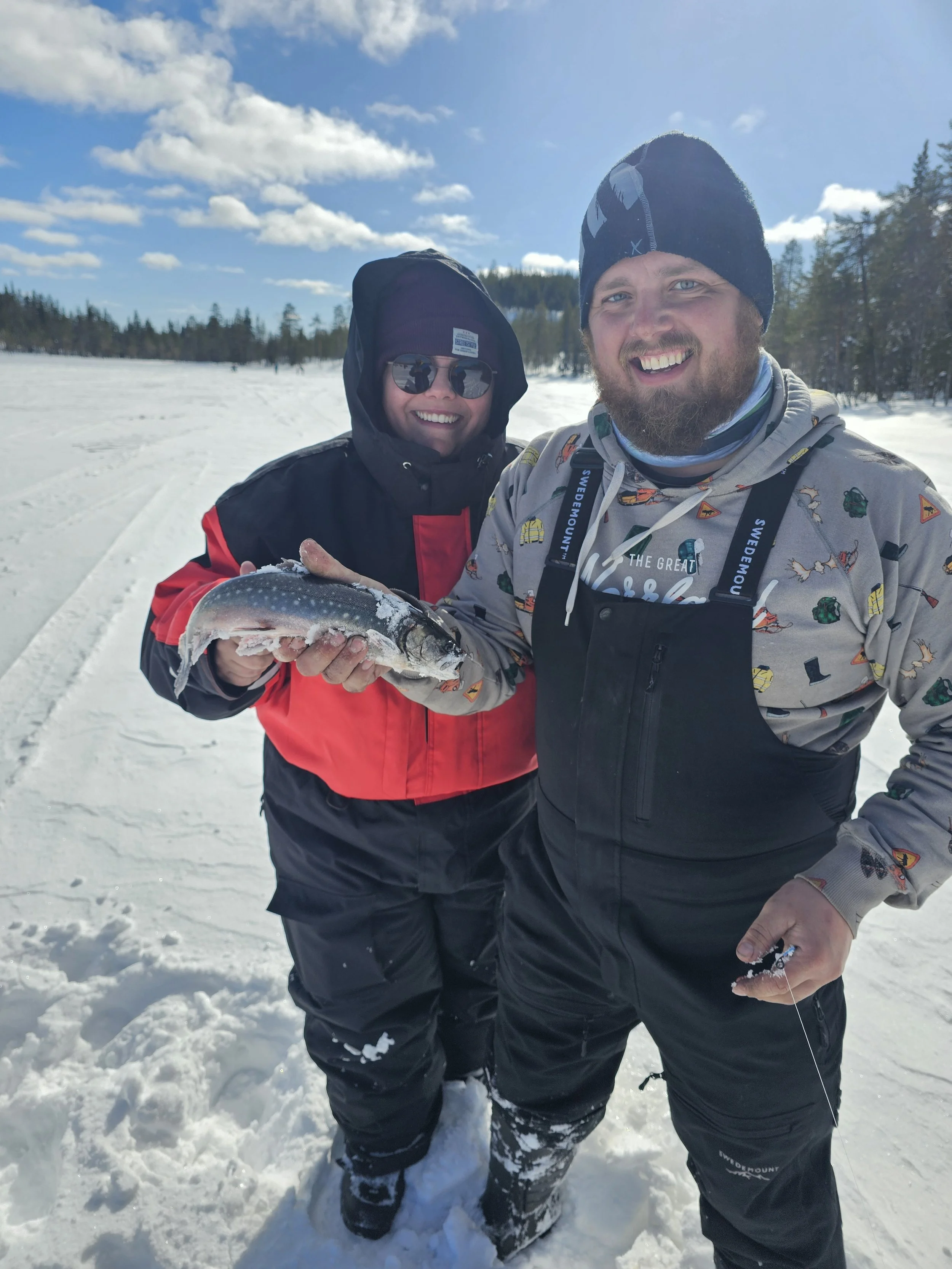 A snowmobile guide and guest smiling as they catch a fish while ice fishing