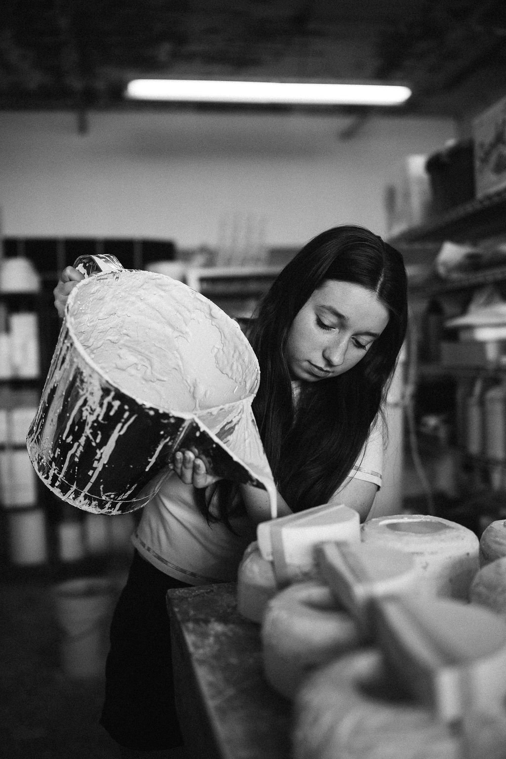  A black and white image of Lauren HB Studio production artist pouring ceramics into molds in the studio 