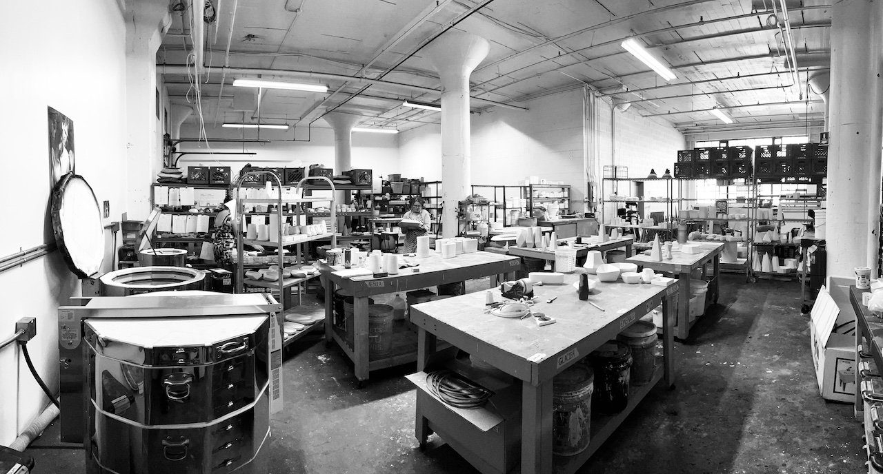  A black and white image of an interior view of Lauren HB Studio with art tables and racks for drying pottery and artwork 