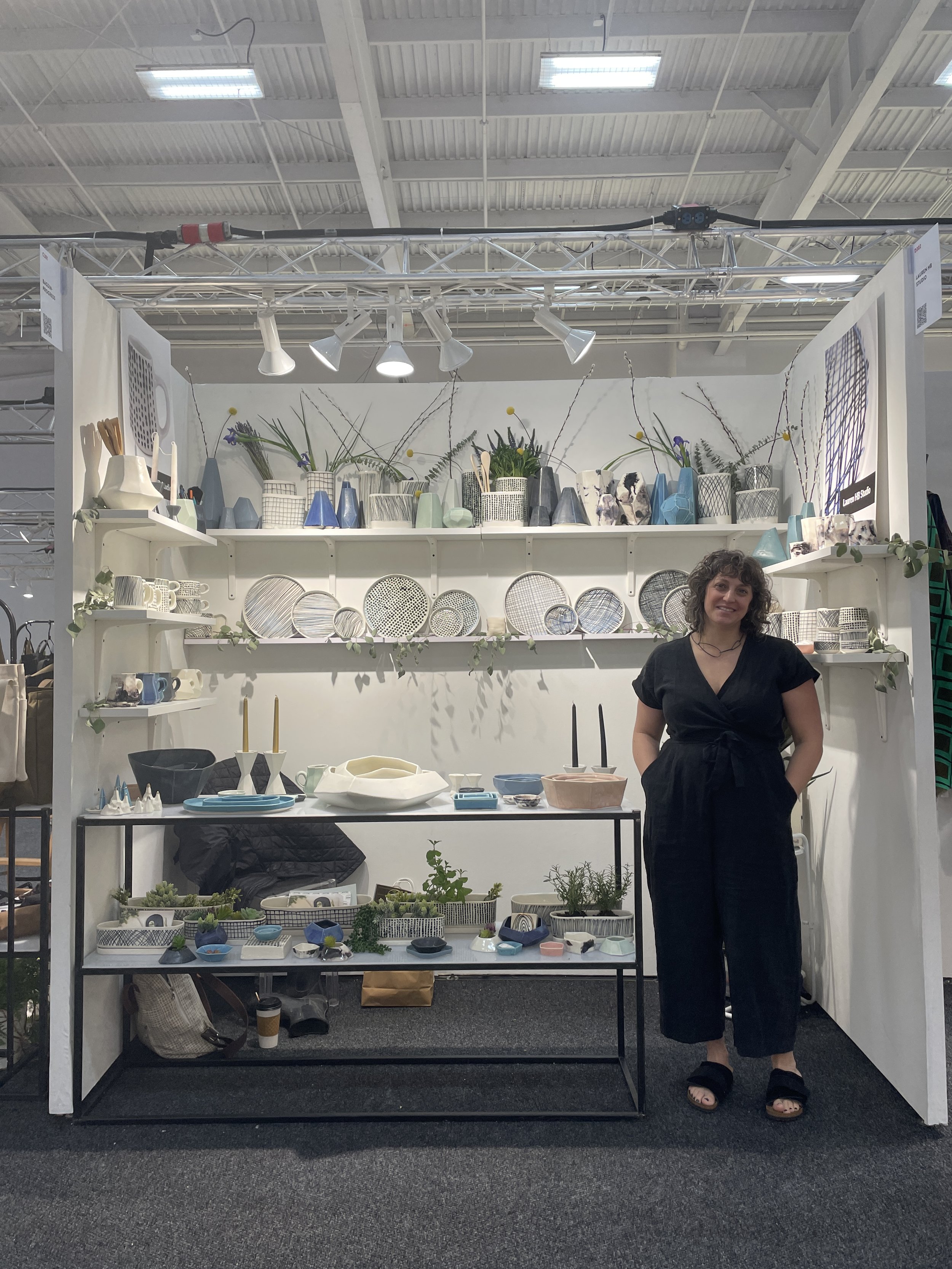  An image of Lauren HB Studio’s founder, Lauren Herzak-Bauman standing in front of Shoppe Object tradeshow display 