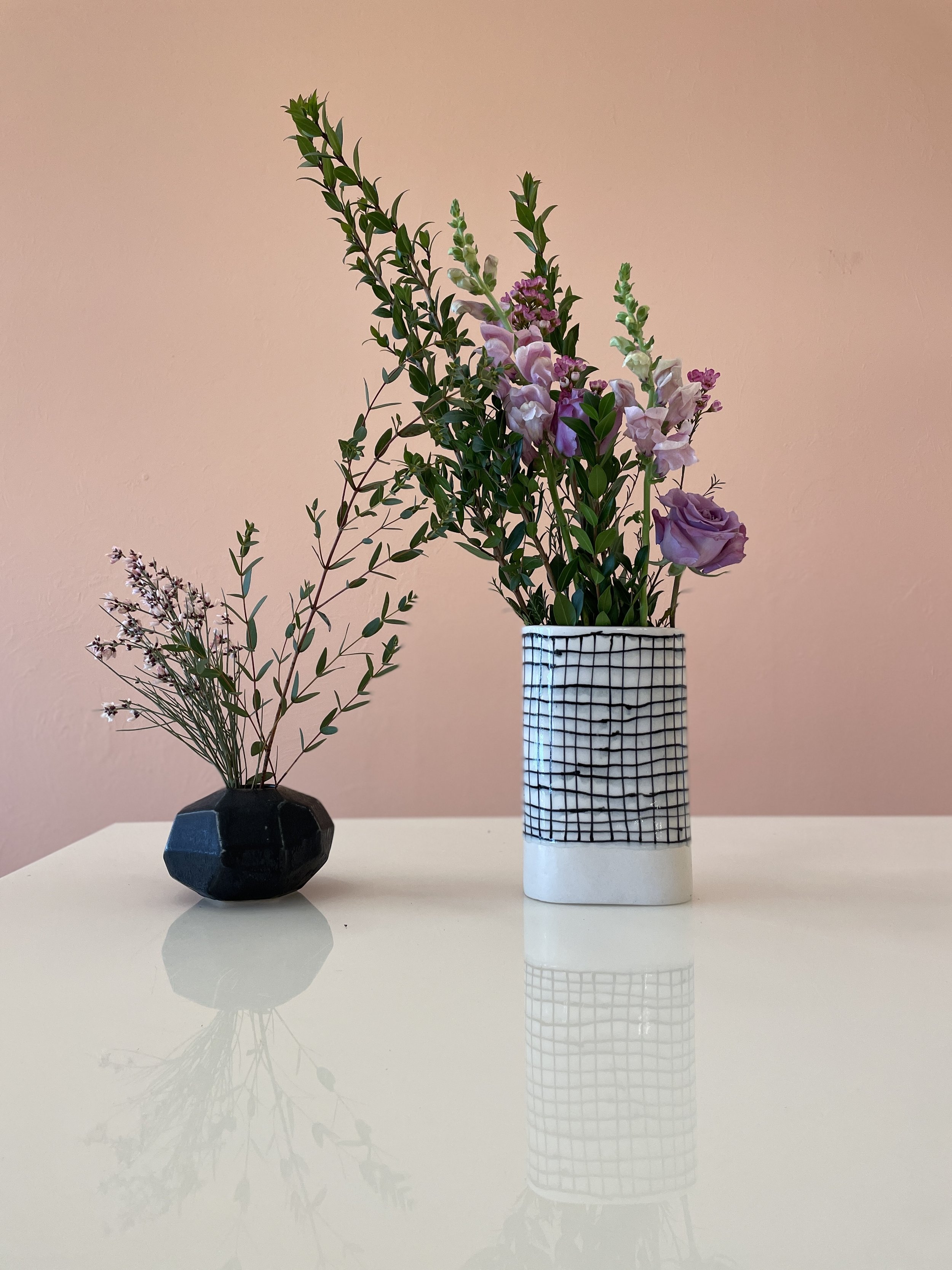  One small, black geometric greenery vase and one tall, white grid design vase with flowers in it made by Lauren HB Studio 