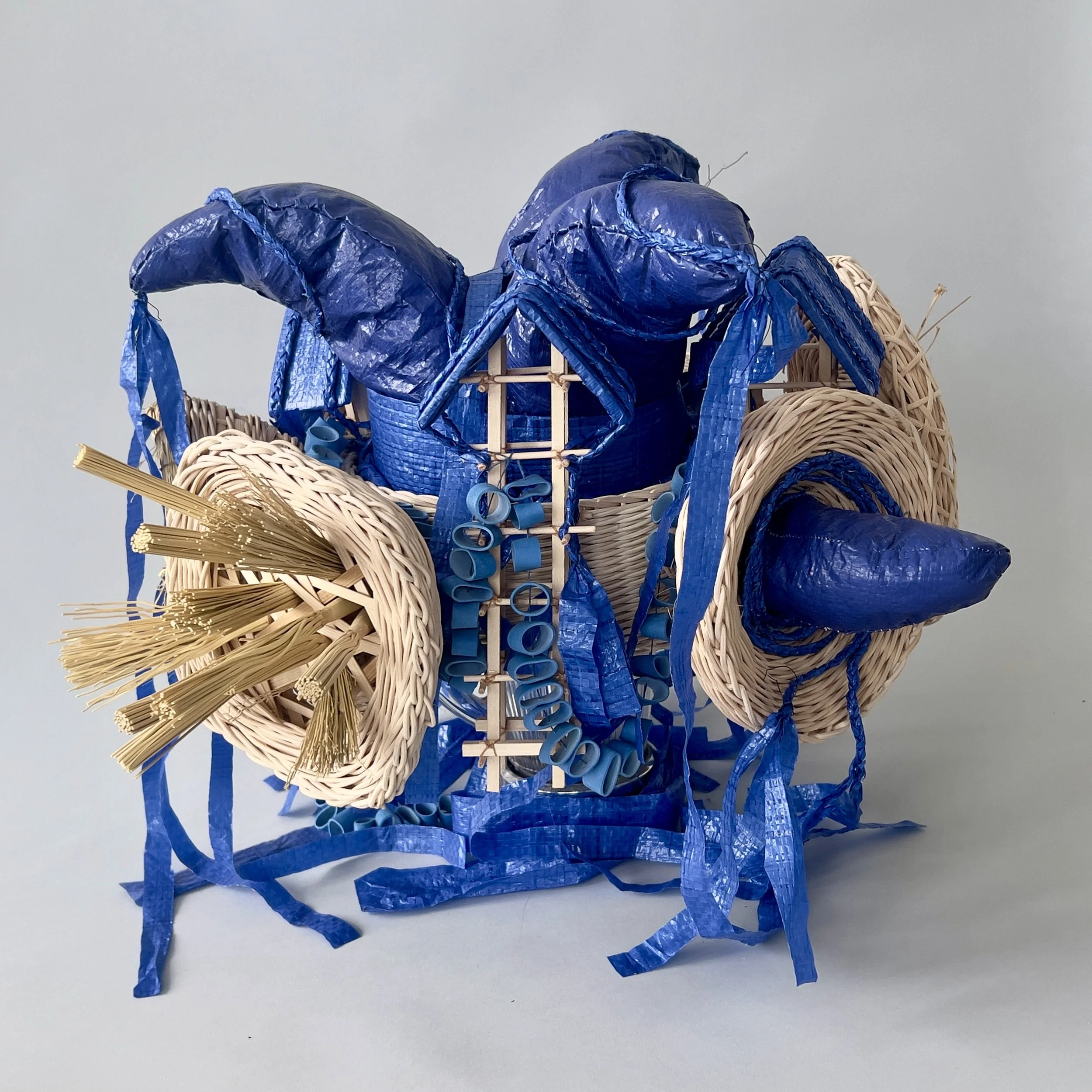 The Queen of Algae / 2026 / Plastic, reed / 16"x18"x15"/ Wearable hat made up of silenced tornado sirens, jester hat and houses for vocal performer in "Love Letters". This head piece is worn by the performer who represents the weather station NOAA St