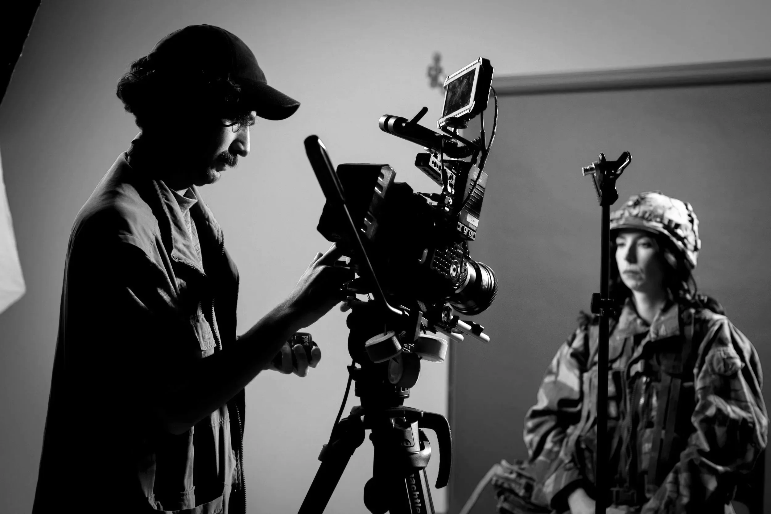A filmmaker operating a professional camera on a shoot with a woman in military camouflage in front of a pink backdrop.
