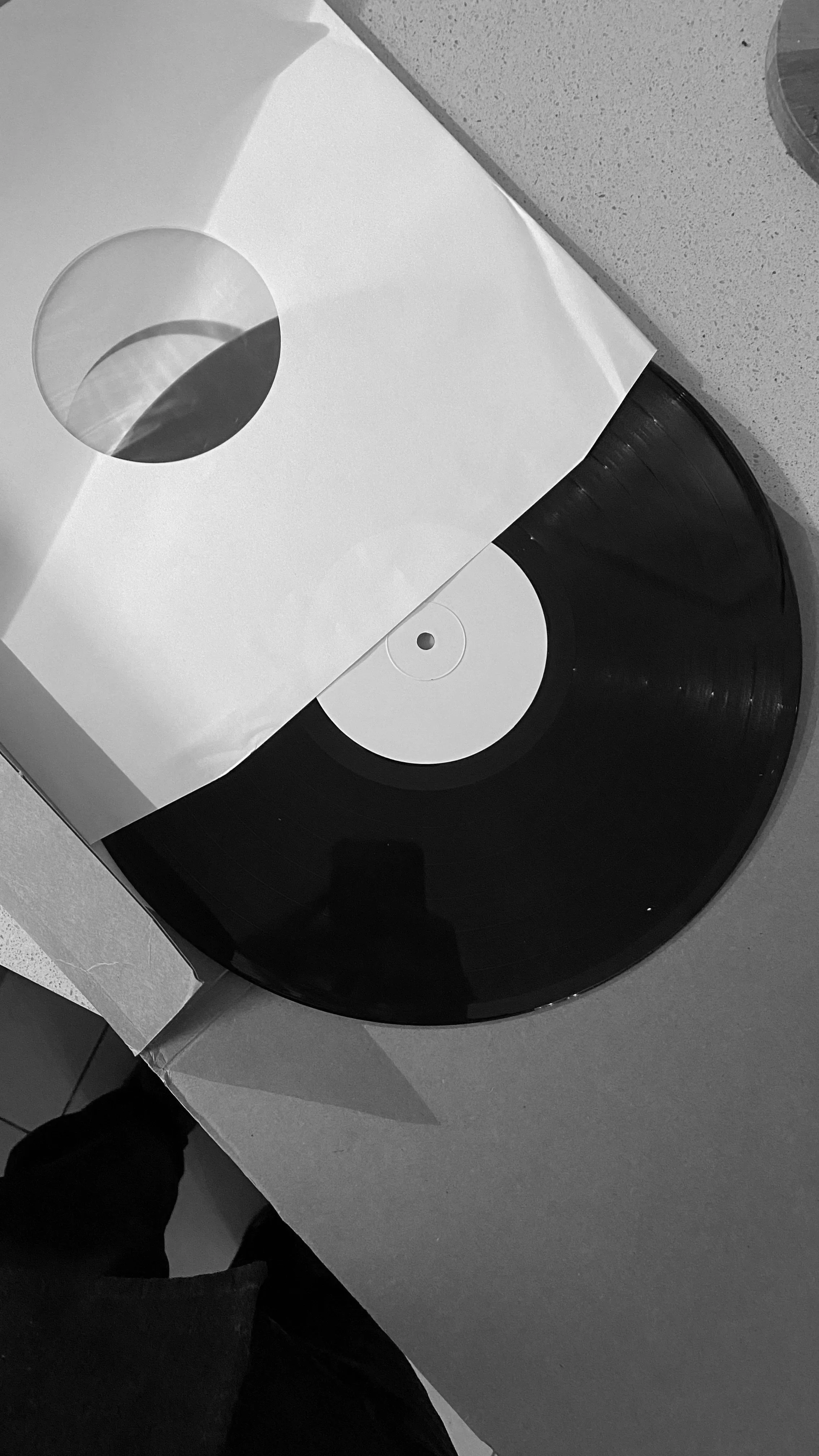 A vinyl record partially inside a white paper sleeve with a hole, resting on a cardboard box on a beige countertop.