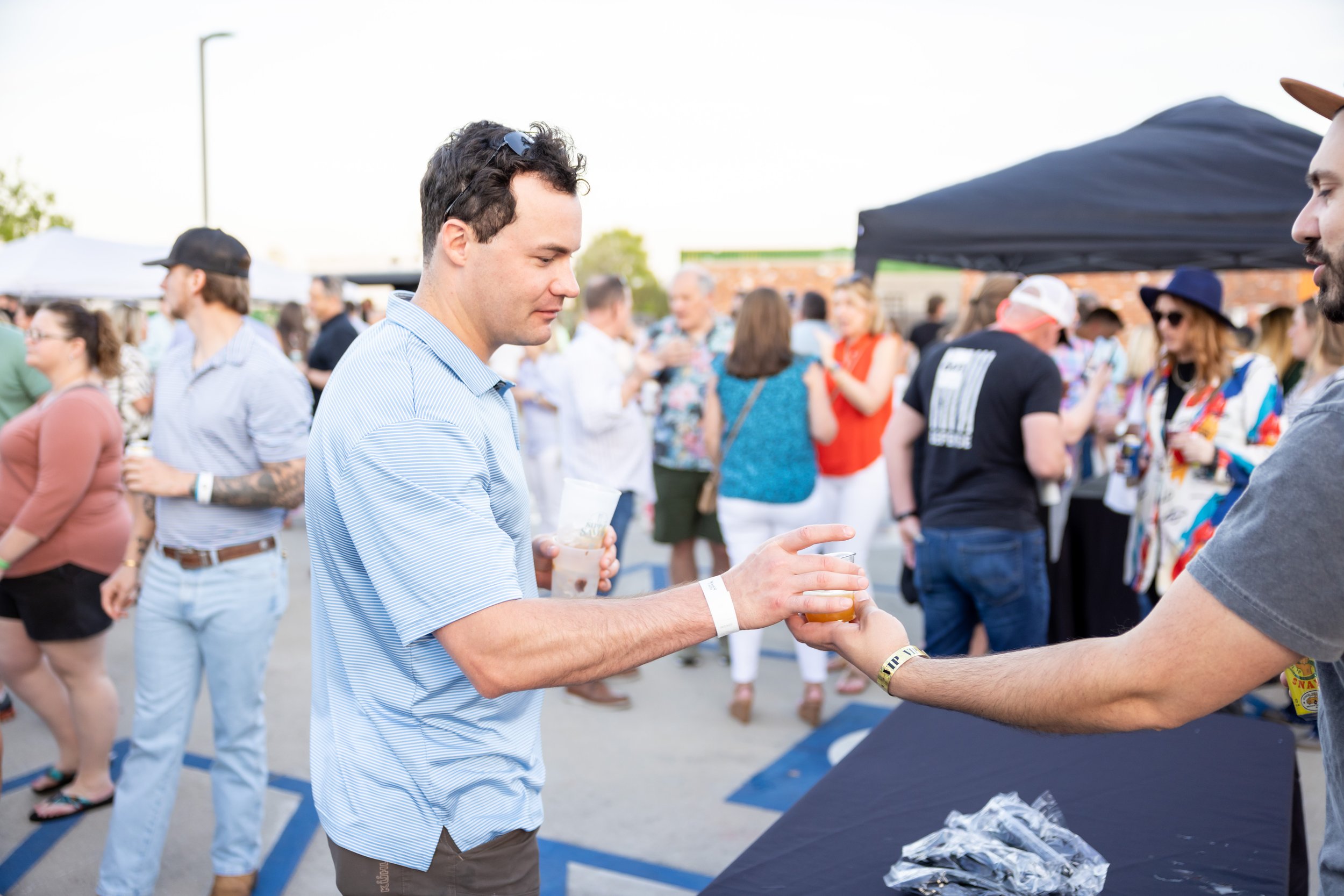 People at an outdoor social event with a person in a blue shirt receiving a drink.