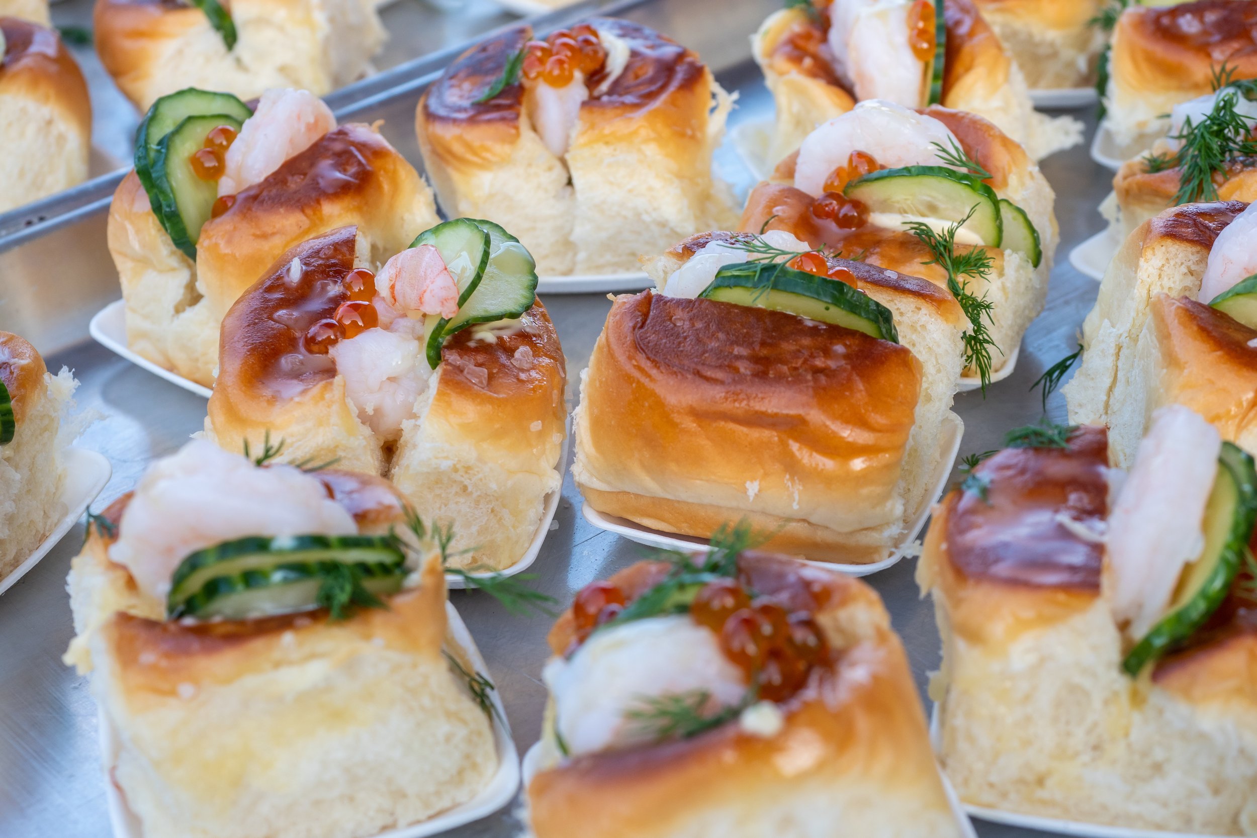 Assorted canapé bites on a tray, topped with cucumber slices, shrimp, smoked salmon, dill, and salmon roe.