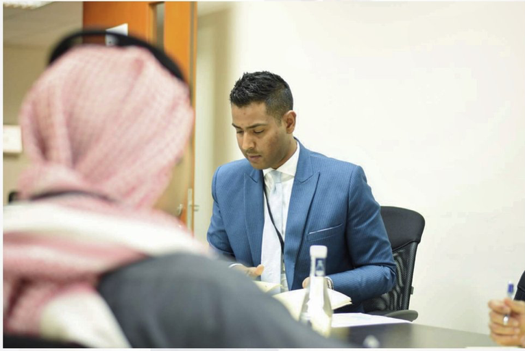 A man in a blue suit and white shirt sitting at a desk, with a woman in traditional Middle Eastern attire in the foreground. Two men in suits shaking hands against a blue background. Bahrain Fahad Aldoseri Aldossari His Excellency Shaikh Khalid bin A