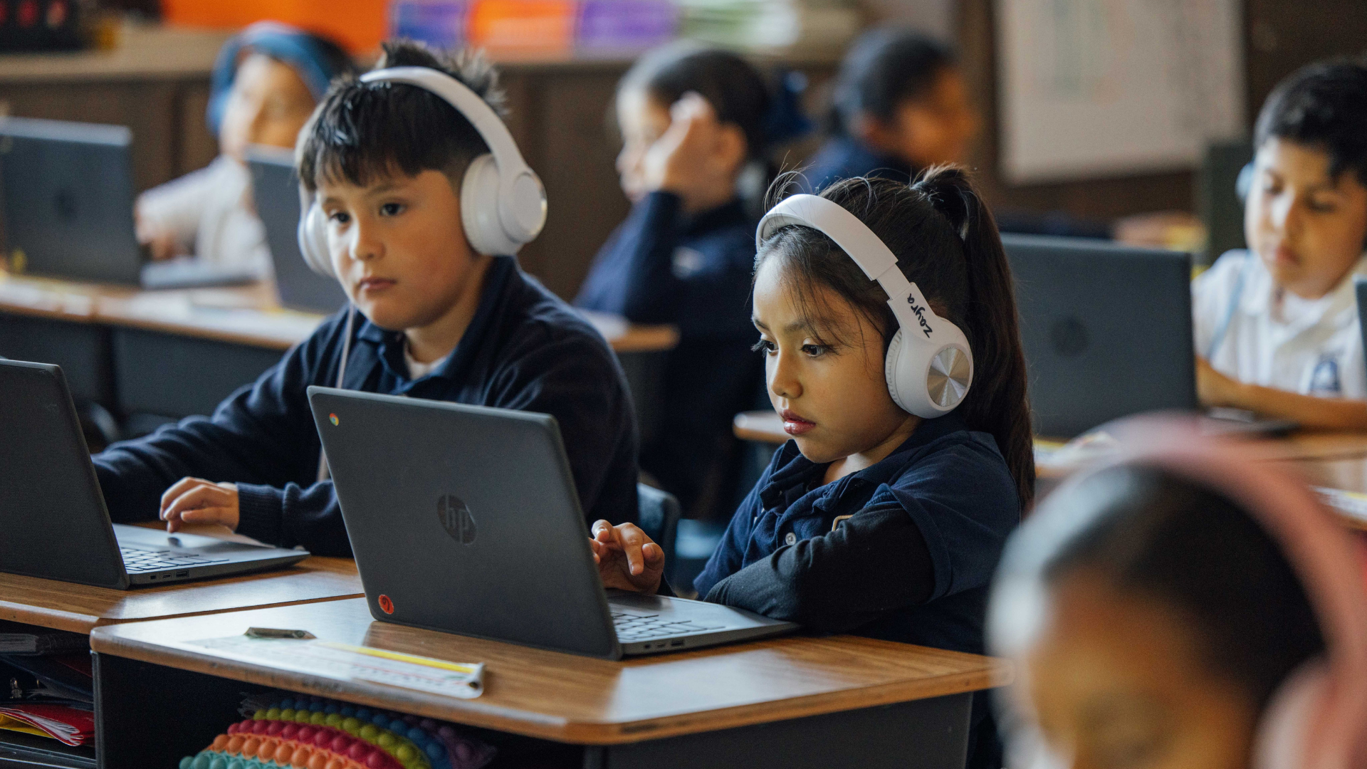 Two students in a classroom use Chromebooks to accompany their learning.