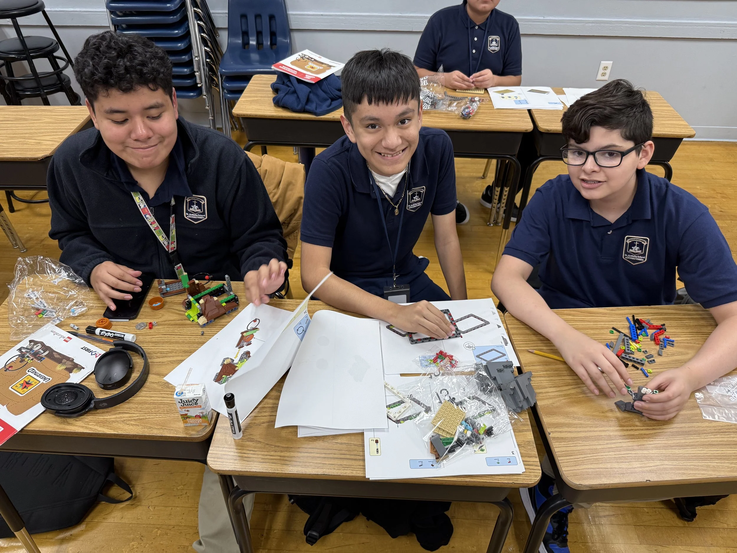 Middle school robotics club students building and programming LEGO sets at a classroom desk, collaborating with guidance from an instructor—highlighting hands-on STEM learning, problem-solving, and innovation at St. Anthony School in Milwaukee, WI.