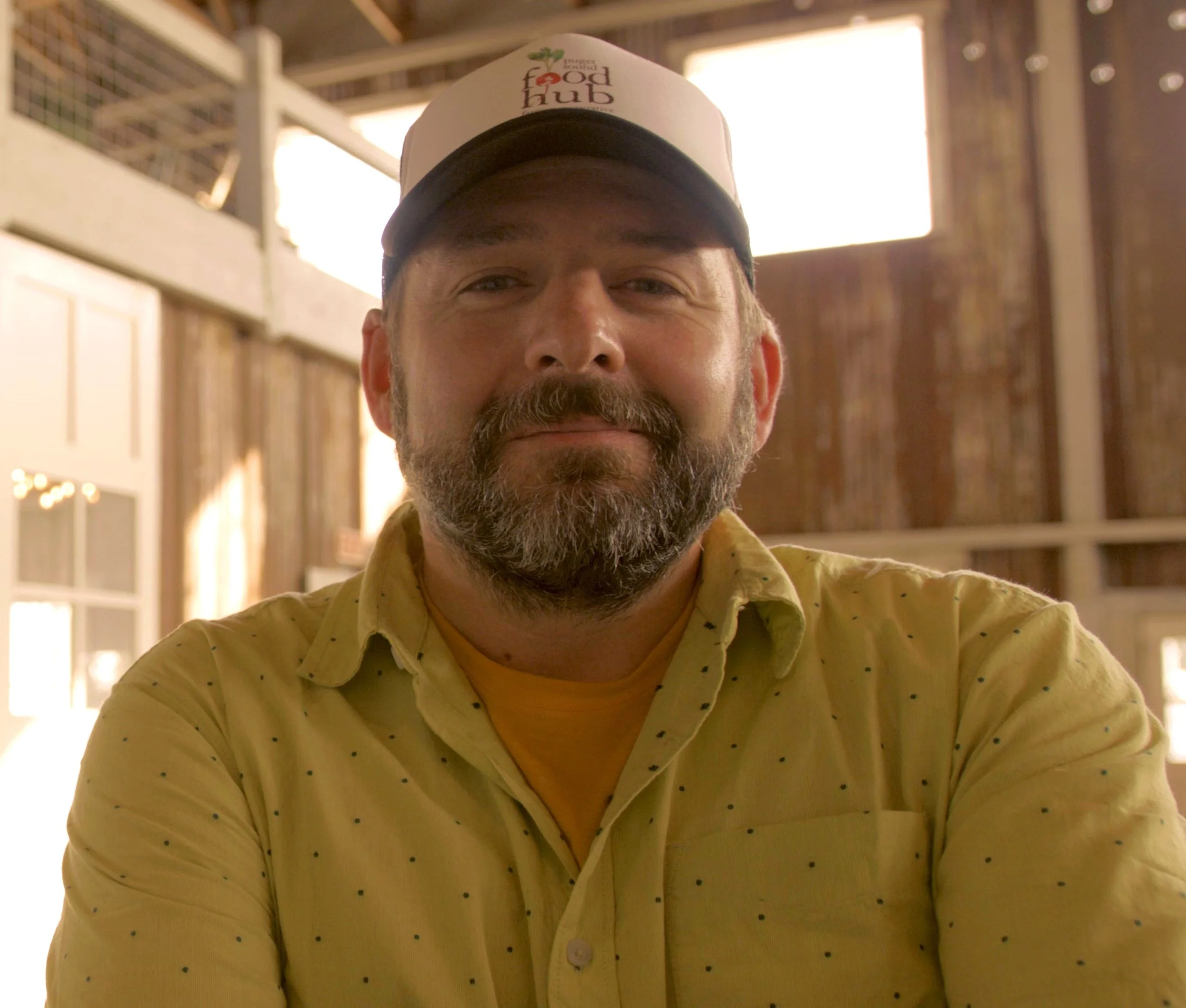 Man wearing a white hat with text, yellow shirt, inside a rustic building.