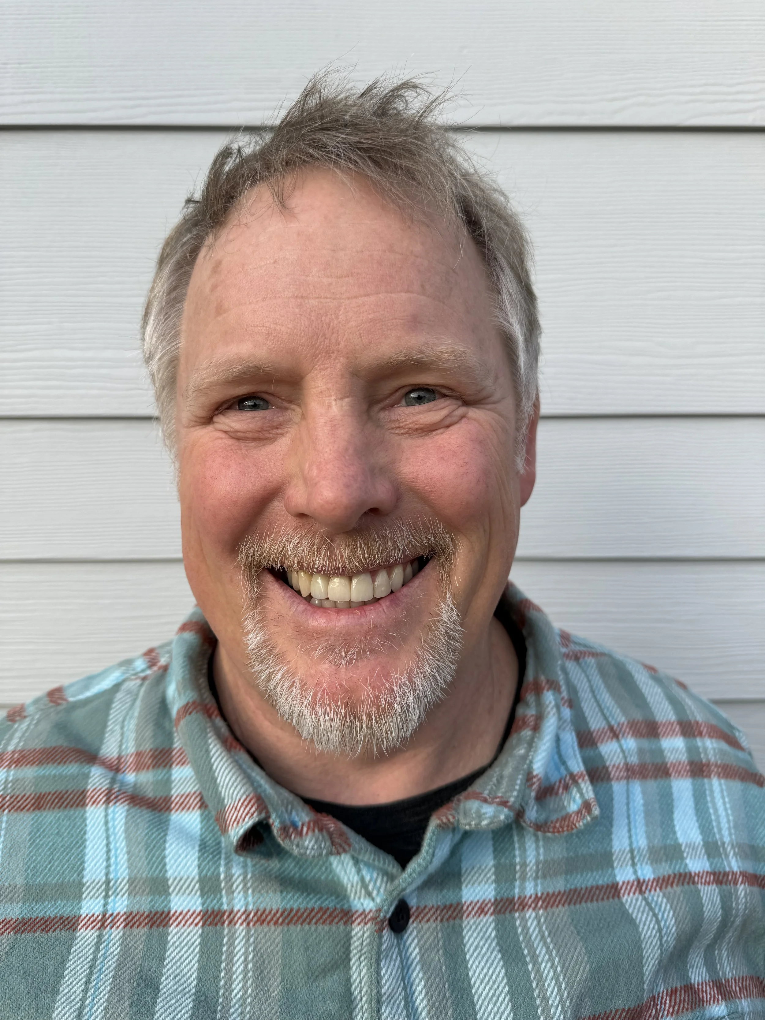 Smiling man in plaid shirt in front of white siding