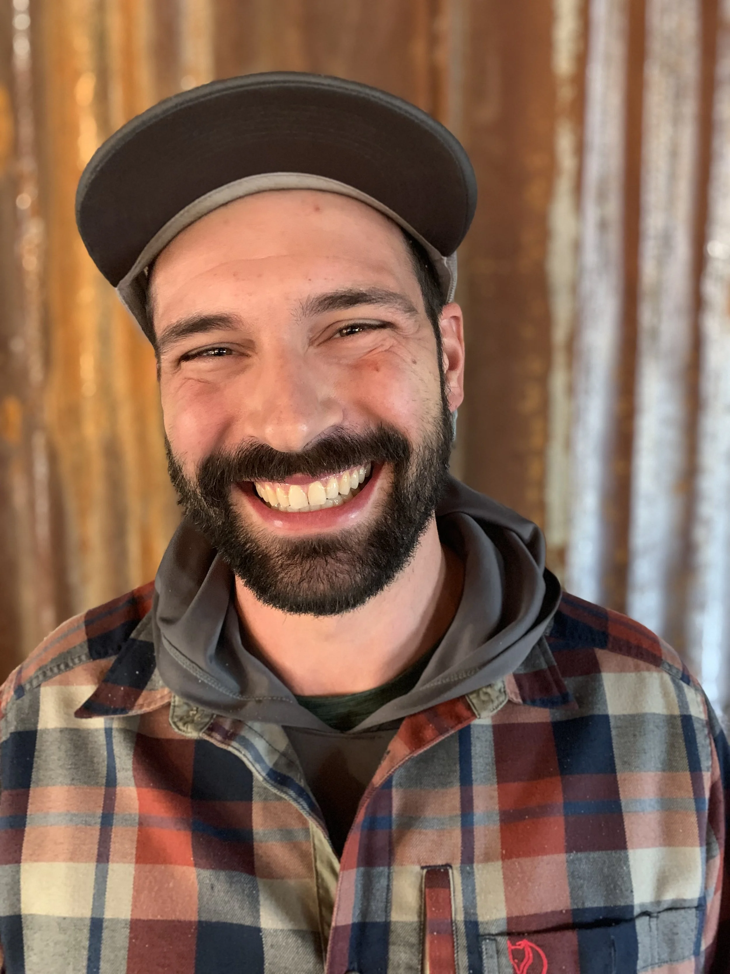 Smiling man wearing a plaid shirt and a cap.