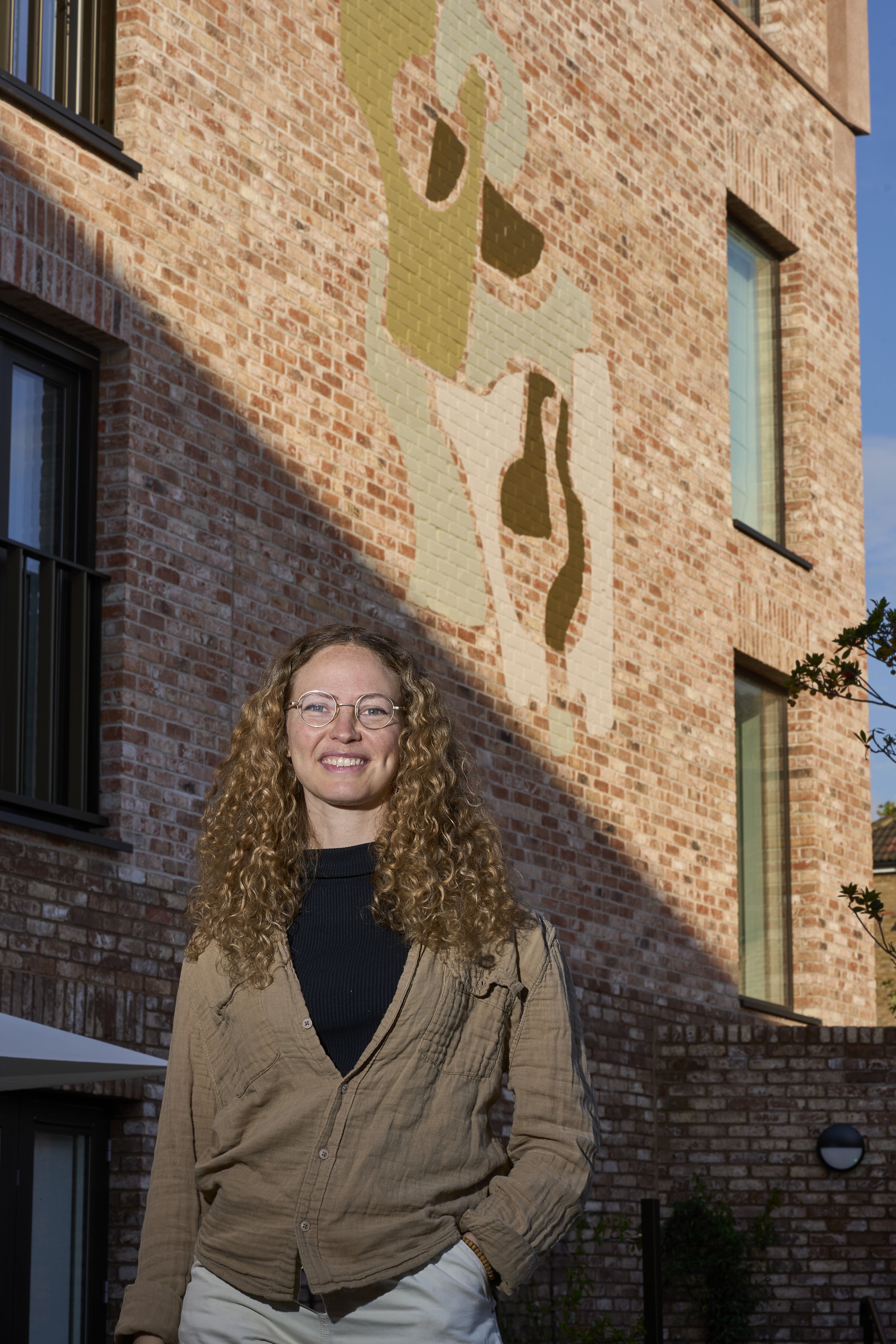 Artist Adriana Jaroslavsky standing in front of her mural Urban Echoes at the Forest Road development in Walthamstow, commissioned and produced by Hive Curates.