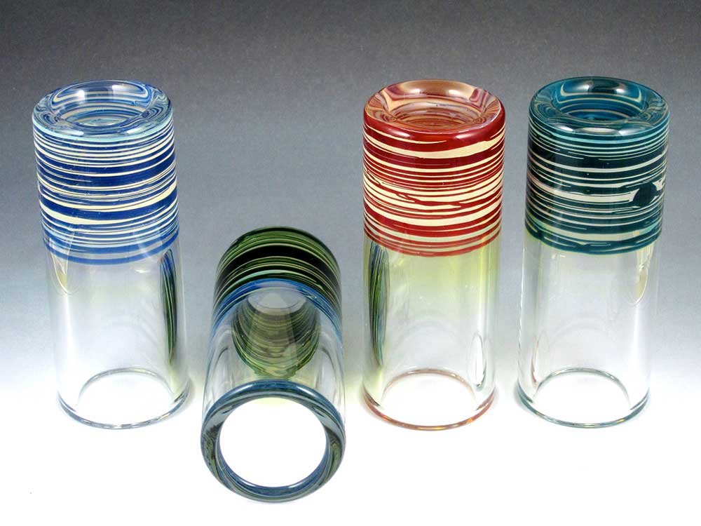 Assortment of handmade heavy wall glass guitar slides with striped blue, red, and teal tops and clear tapered bodies.
