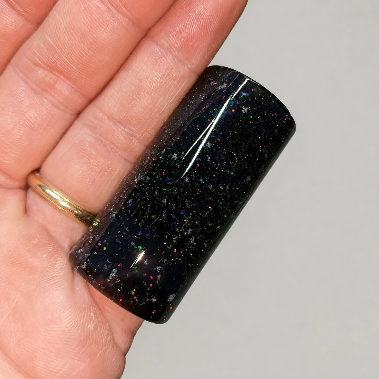 Crushed Opal #2 handmade black glass guitar slide with multicolor synthetic opal shown in hand