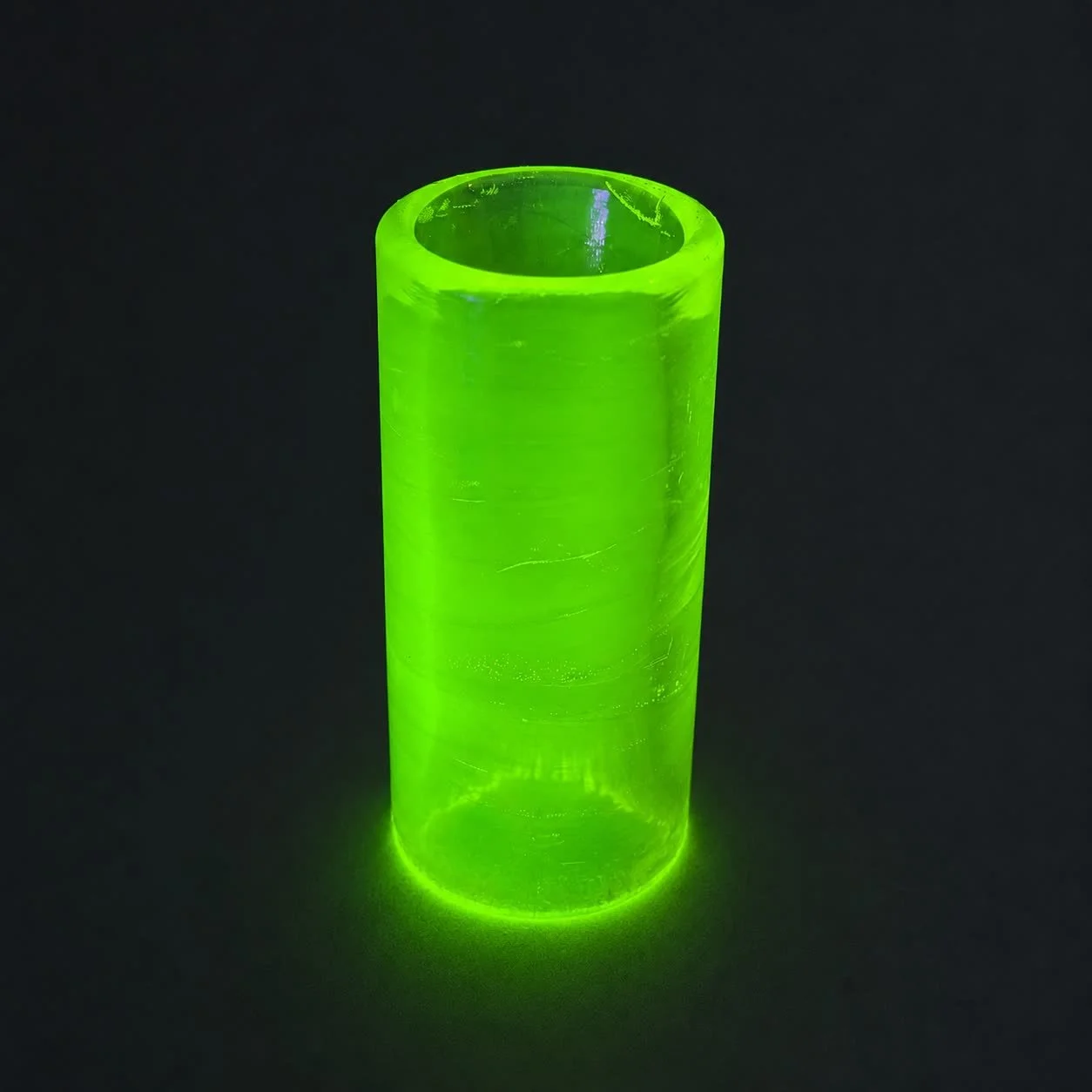 Blacklight Glow #1 glass guitar slide standing upright and glowing neon green under UV light