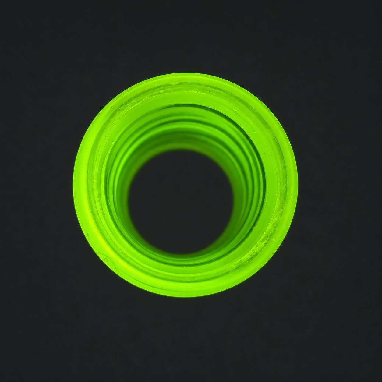 End view of Blacklight Glow #2 non-tapered glass guitar slide fluorescing under UV light
