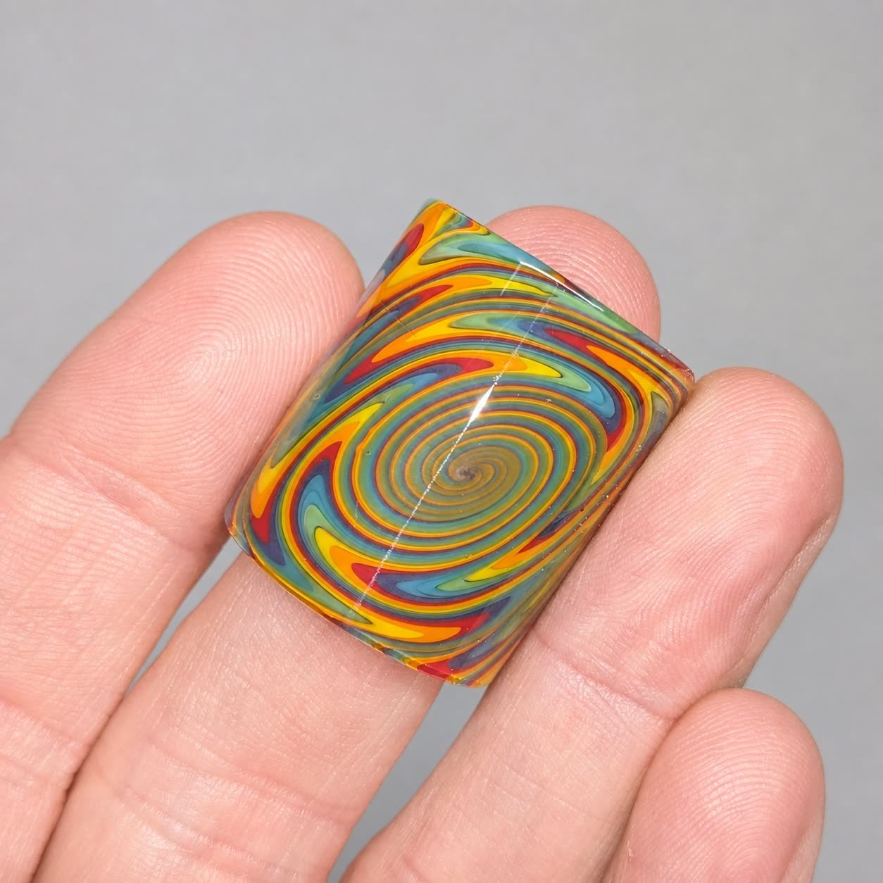 Tie Dye Spiral Mini handmade glass guitar slide with vivid multicolor spiral pattern shown on hand