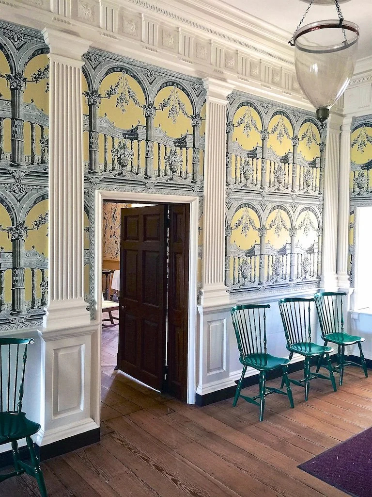 The central passage is lined by six symmetrical Doric-style pilasters. The front of the hall is covered in wallpaper.
