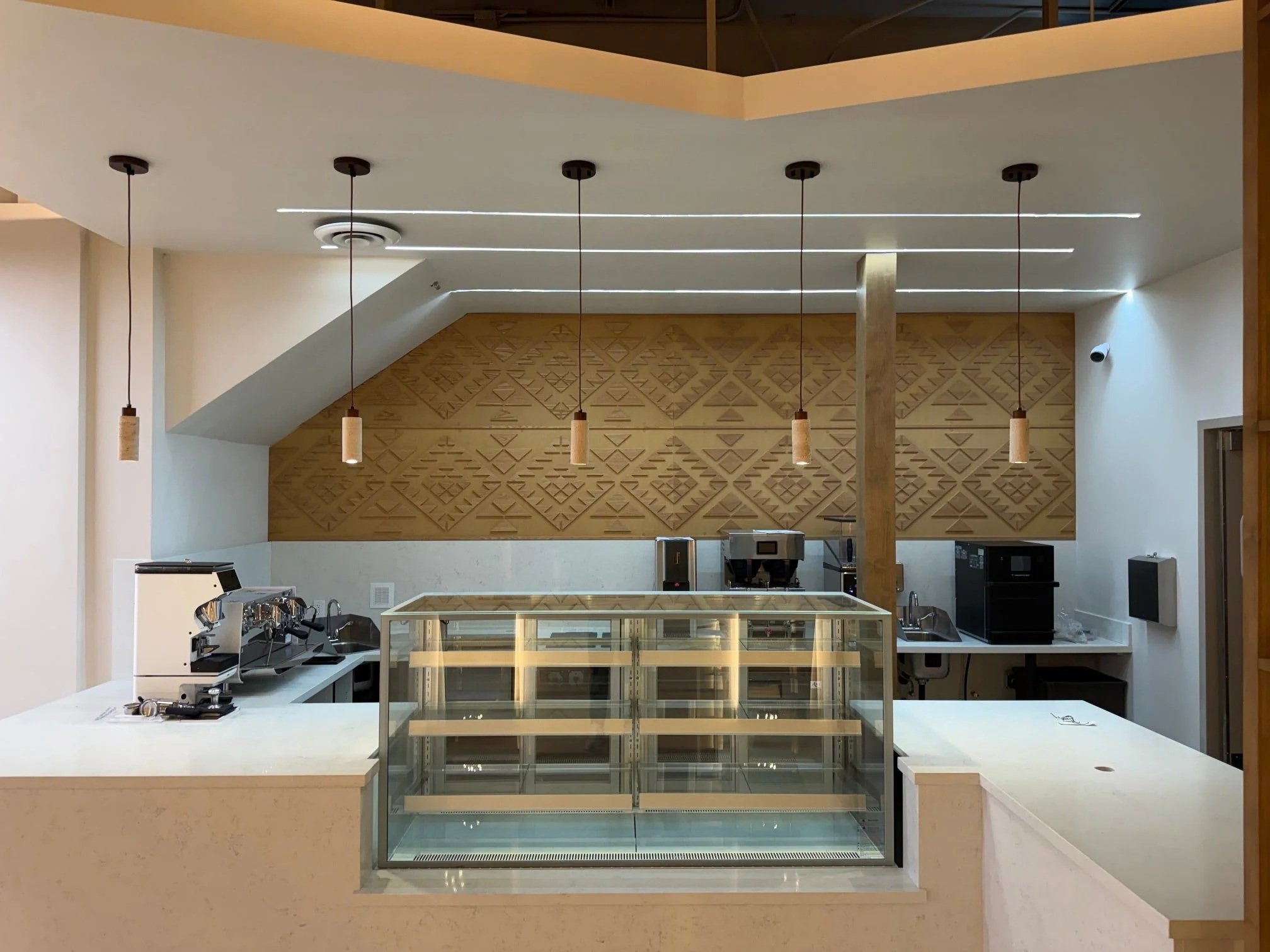 A coffee shop counter and glass display case. There's an intricately-etched sheet of MDF on the wall behind the counter.