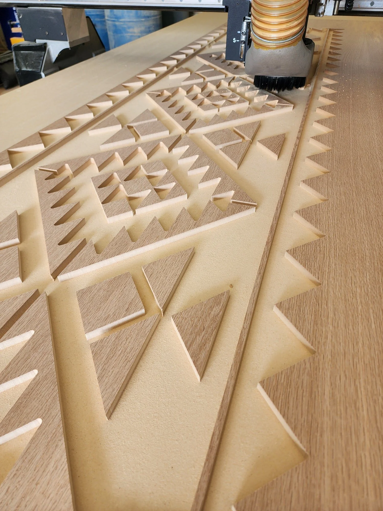 A machine carving a geometric design into a sheet of wood